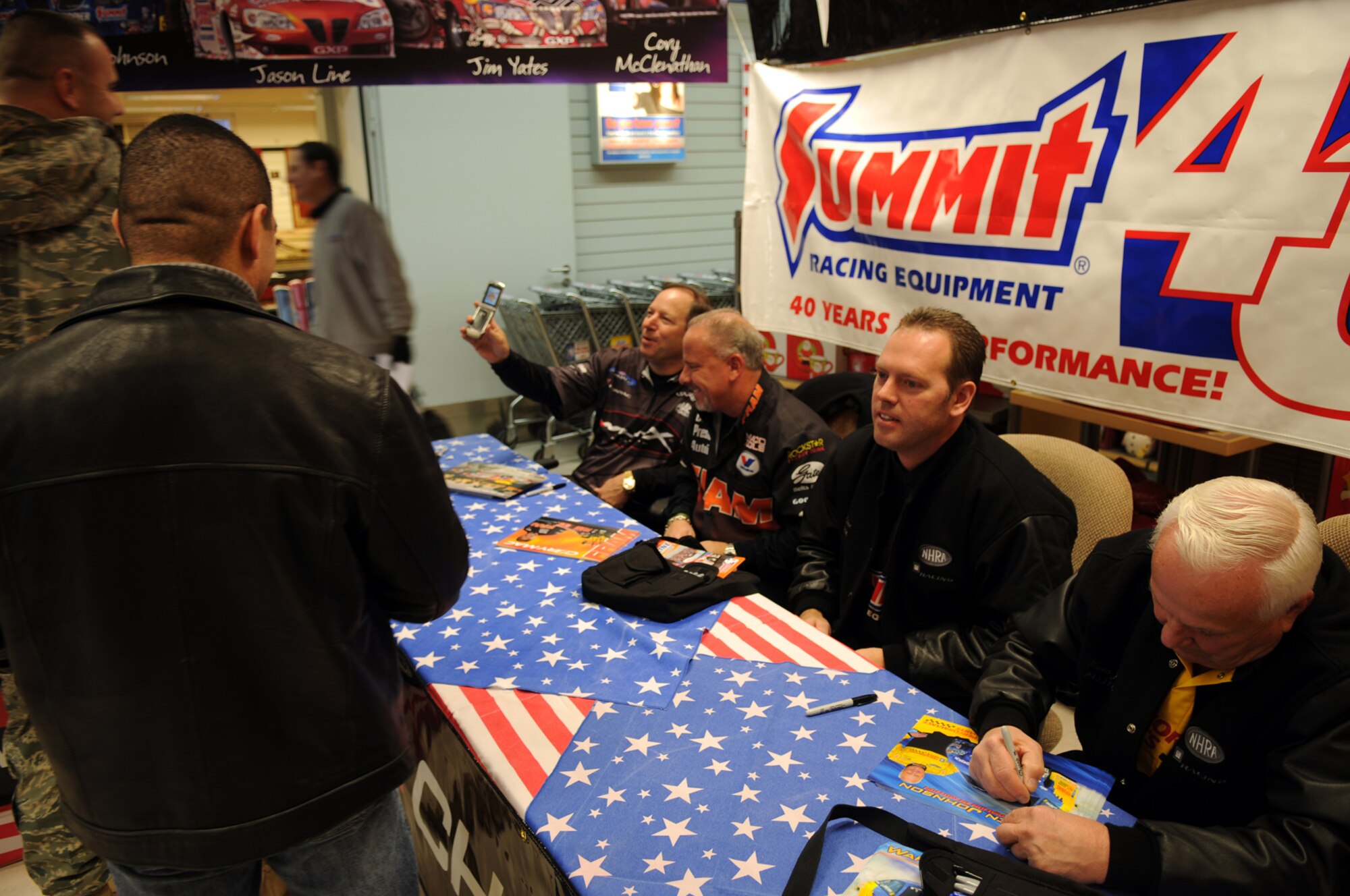 Four drivers from the National Hot Rod Association sign autographs and talk to servicemembers at the Vogelweh Base Exchange, during a USO sponsored trip, Ramstein Air Base, Germany, Nov. 25, 2008. The drivers are on the second leg of their trip after coming from Kuwait to visit American service members early that morning. (Airman 1st Class Scott Saldukas)
