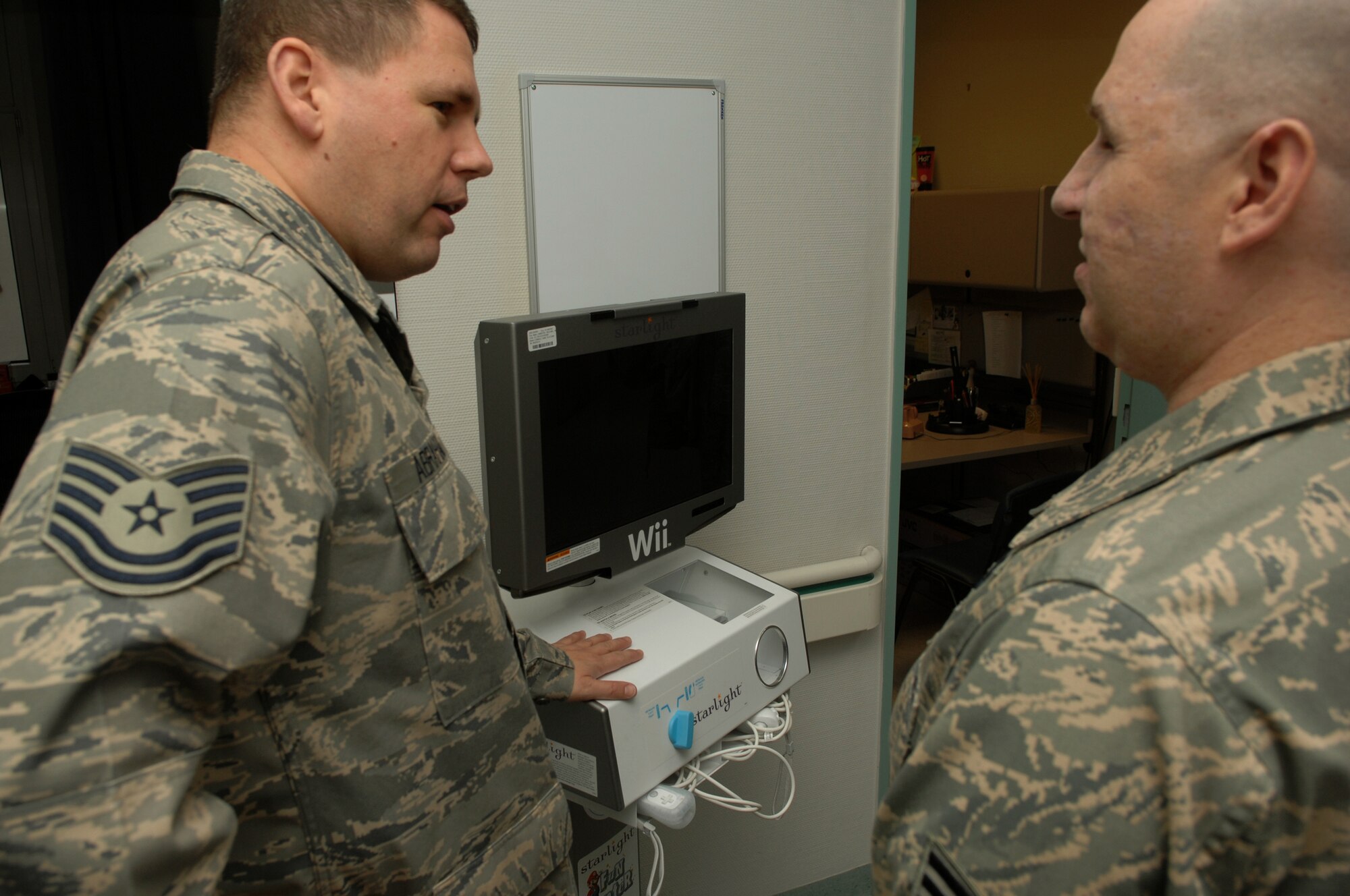 Tech. Sgt. Paul Abraham, Medical Surgery noncommissioned officer in charge, shows off the new Nintendo Wii donated to the ward by Army & Air Forces Exchange Service, to Staff Sgt. Matthew Slaydon, explaining that the game system is used as a physical rehabilitation aid for injured patients, Landstuhl Regional Medical Center, Germany, Nov. 21, 2008. Sgt. Slaydon was severely injured in Iraq 13 months ago during a deployment there as an explosive ordinance disposal technician and is visiting LRMC as part of a morale tour, following his recovery. (U.S. Air Force photo by Airman 1st Class Tony R. Ritter)