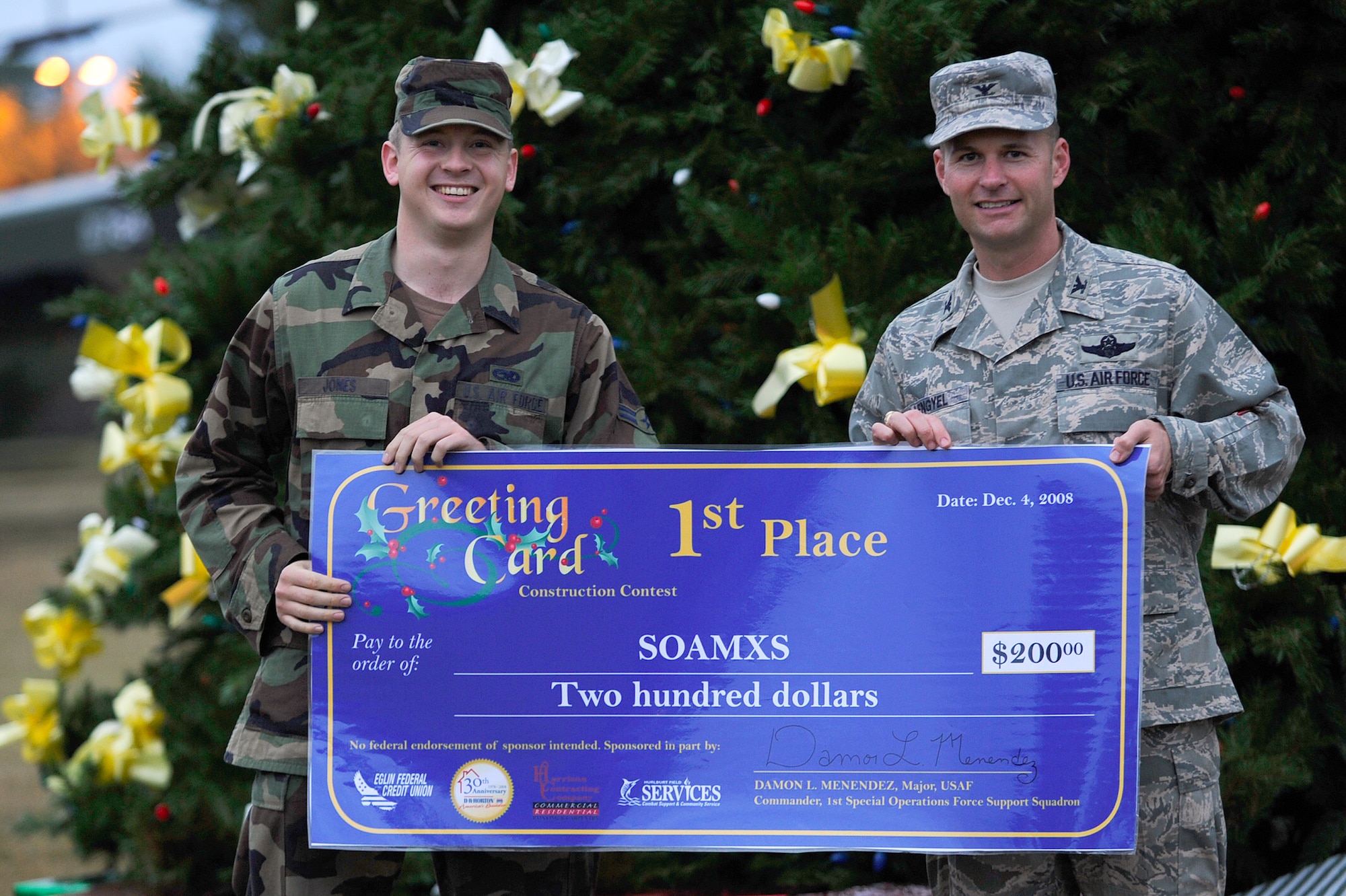 Col. Greg Lengyel, 1st Special Operations Wing commander, presents a big check for two hundred dollars to Airman 1st Class Sean Jones, 15th Aircraft Maintenance Unit crew chief, for winning first place in the holiday greeting card contest Dec. 4. The oversized greeting cards are created by respective units and on display at the main entrance to the base. (U.S. Air Force Photo/Senior Airman Julianne Showalter)