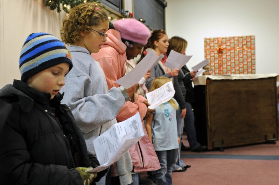 Military dependents sing holiday songs during the annual holiday tree lighting ceremony here, Dec. 4. After the tree was lit, Airmen and their families enjoyed snacks, carols, and time with Santa at the Freedom Chapel Annex. (US Air Force photo/Airman Corey Hook)