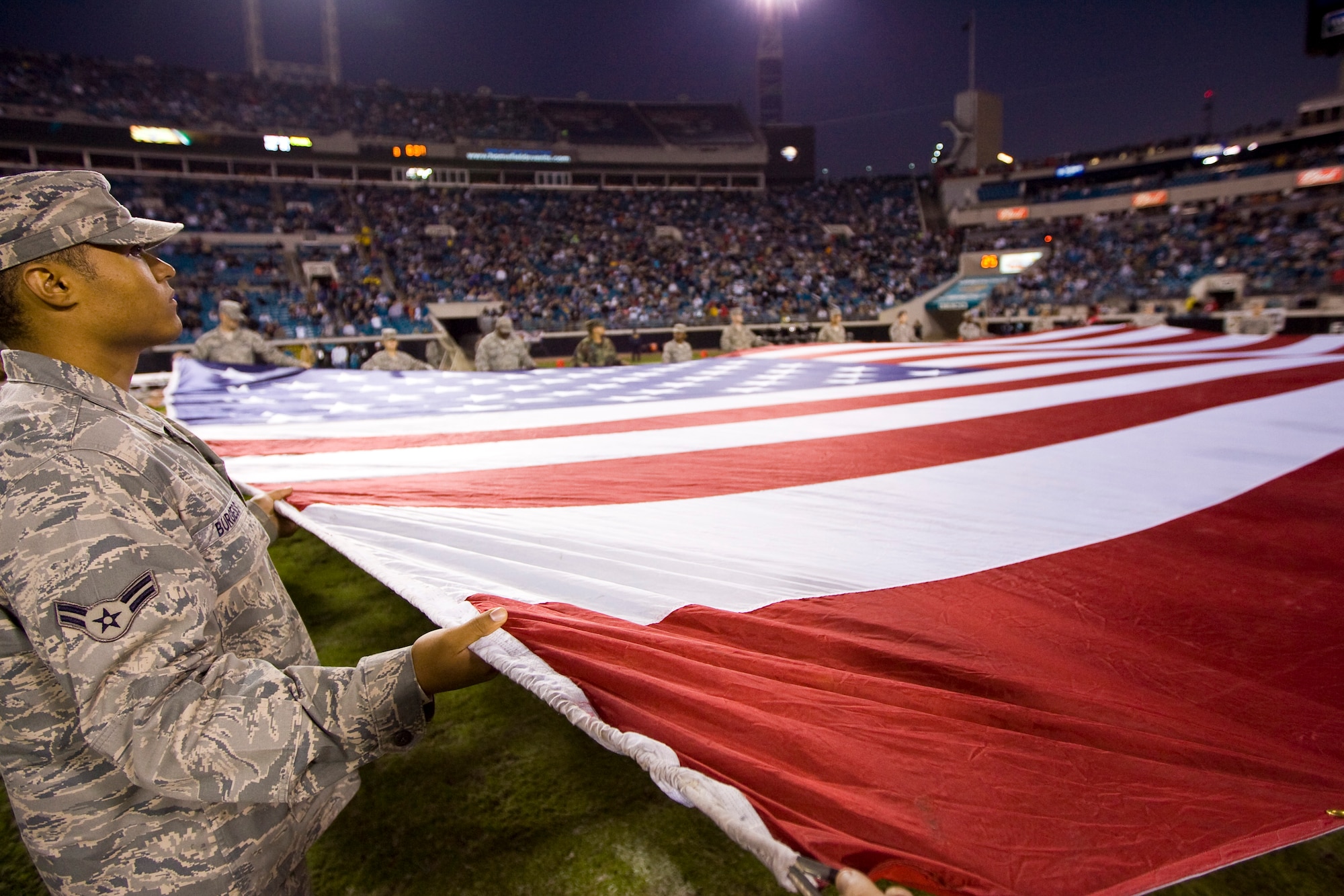 Airman First Class Brian Burgess of the 325th Air Control Squadron holds the edge of the American Flag on the field of the Jacksonville Jaguars during the singing of the National Anthem Nov. 16. More than 65 Tyndall Airmen, who were joined by other soldiers, sailors and marines stationed along the Florida Panhandle, participated in Military Appreciation Day by displaying a football field sized flag.  (Photo by Paul Figura) 
 
