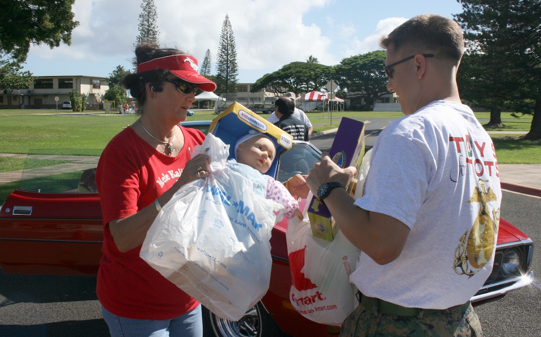 Pam West, of the Aloha Mustang and Shelby Club, hands toy donations to Gunnery Sgt. Chris Whitley, Toys for Tots Coordinator, at the 34th Annual Oahu Car Clubs Toy Cruise donation site aboard MCBH.  More than 200 drivers from a variety of car clubs from around the island donated more than 700 toys at the end of the annual cross-island cruise.
