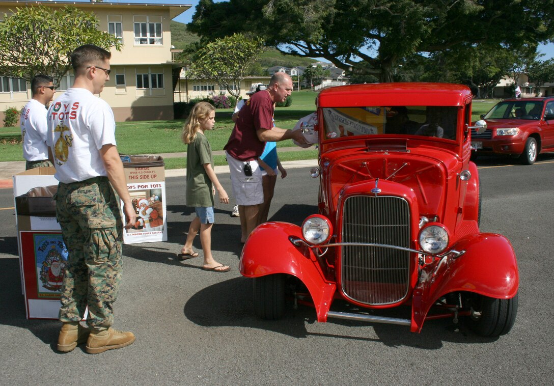 Kingston Liao, driving his '32 Ford, drops off toy donations with Col. Robert Rice, Base Commander, MCBH, and Kathleen White, the 9-year-old daughter of Col. Duffy White, 3rd Marine Regimental Commander, as Gunnery Sgt. Chris Whitley and Staff Sgt. Marco Garcia, 4th Force Reconnaissance Company, wait to load them into donation boxes.  Car clubs rallied aboard base at the end of the 34th Anuual Oahu Car Club Toy Cruise from Kapolei to MCBH.  More than 200 drivers from a variety of car clubs from around the island donated more than 700 toys during the annual cross-island cruise.
