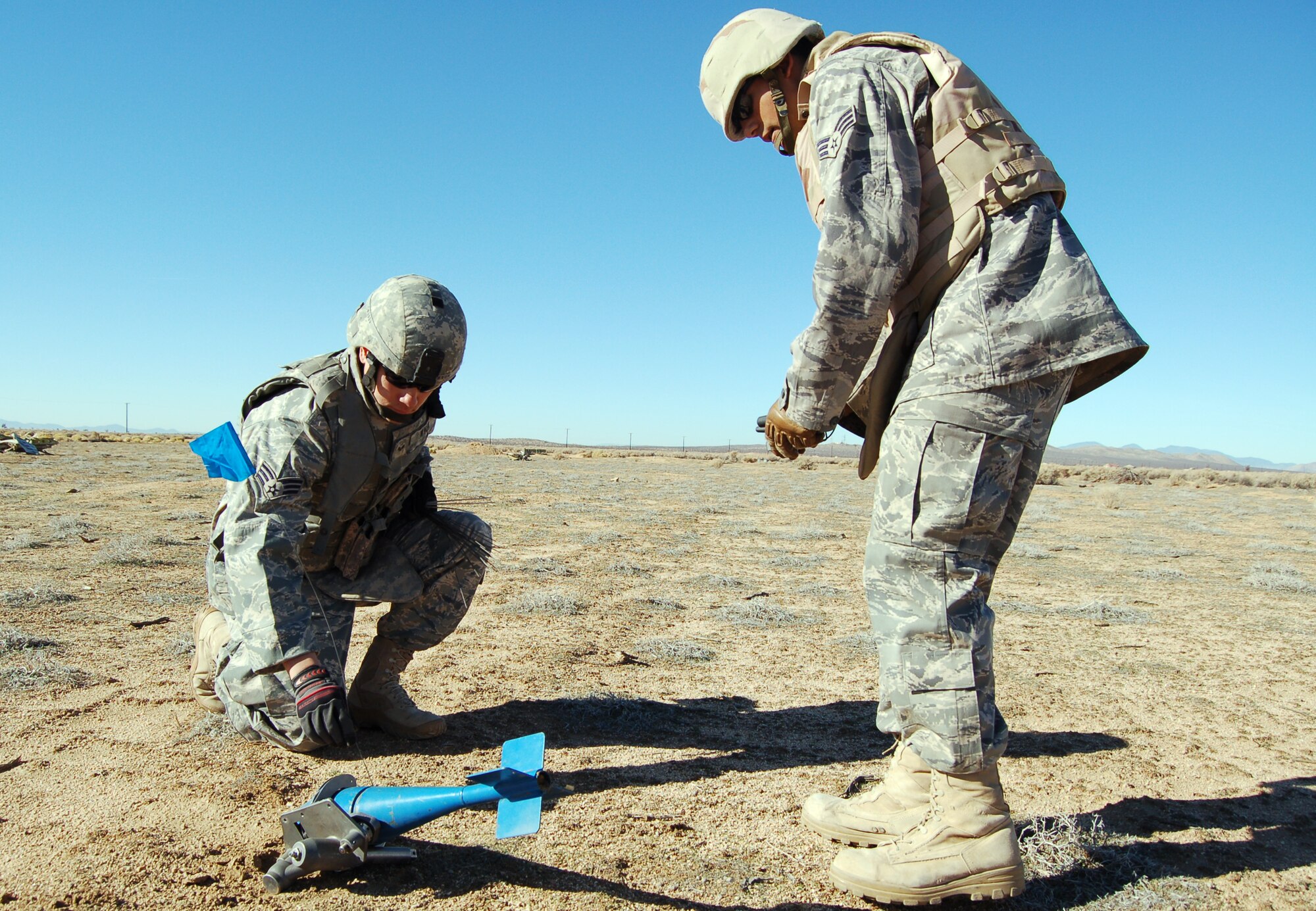 Senior Airman Oscar Ortega (right), Explosive Ordnance Disposal Unit technician, and Senior Airman Christopher Wnuk, EOD journeyman, mark an unexploded ordnance during an Emergency Management Exercise Dec. 3 at Camp Corum. (Air Force photo by Senior Airman Julius Delos Reyes)