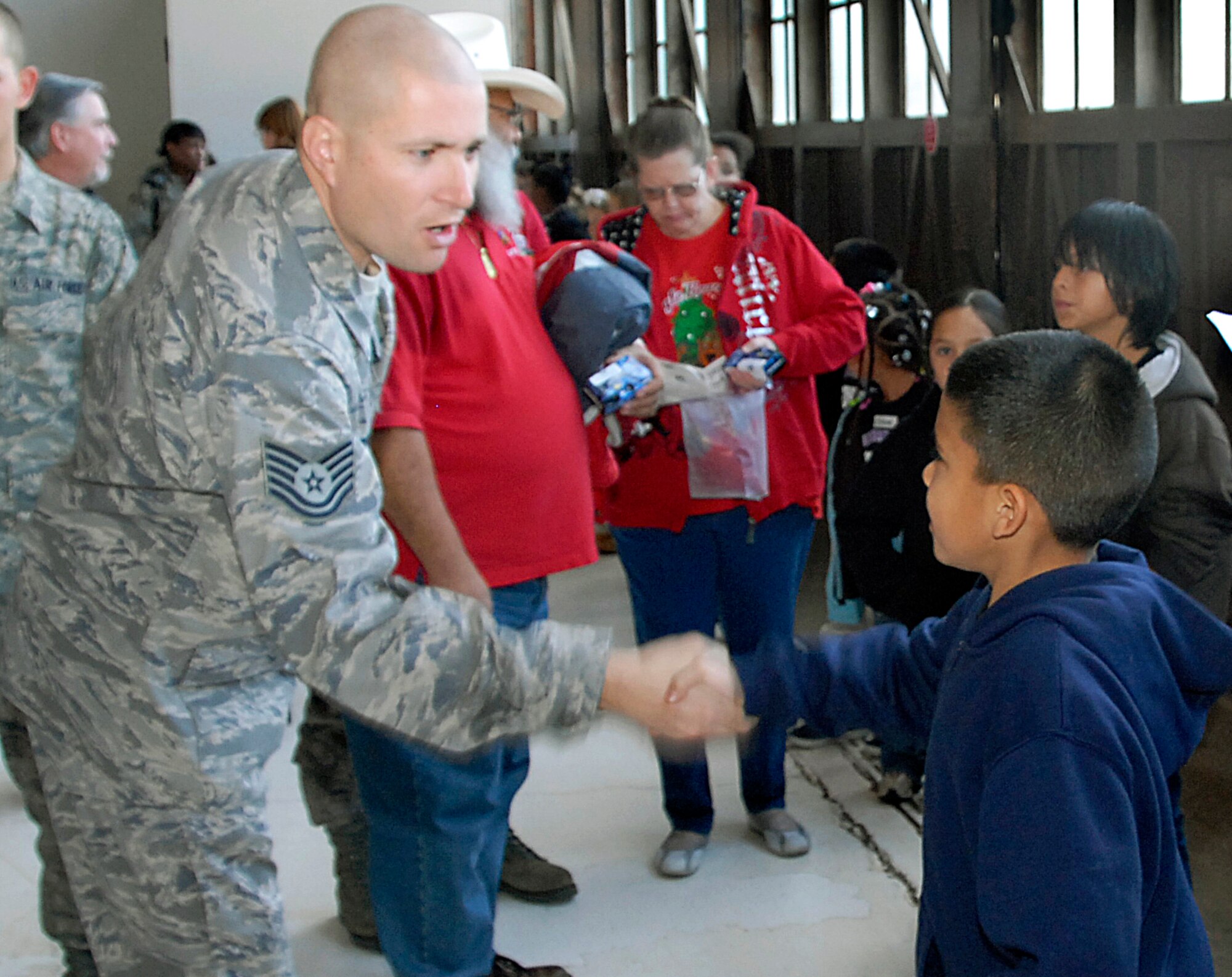 Tech. Sgt. Toby Roach, a munitions instructor for the 363rd Training Squadron, shakes hands with Ricardo Deleon, a 3rd grader at Southern Hills Elementary school. Roach acted as Deleon's sponsor for the afternoon at the Give a Child a Christmas held in Hangar 1090 Dec. 5. (U.S. Air Force photo/Harry Tonemah)