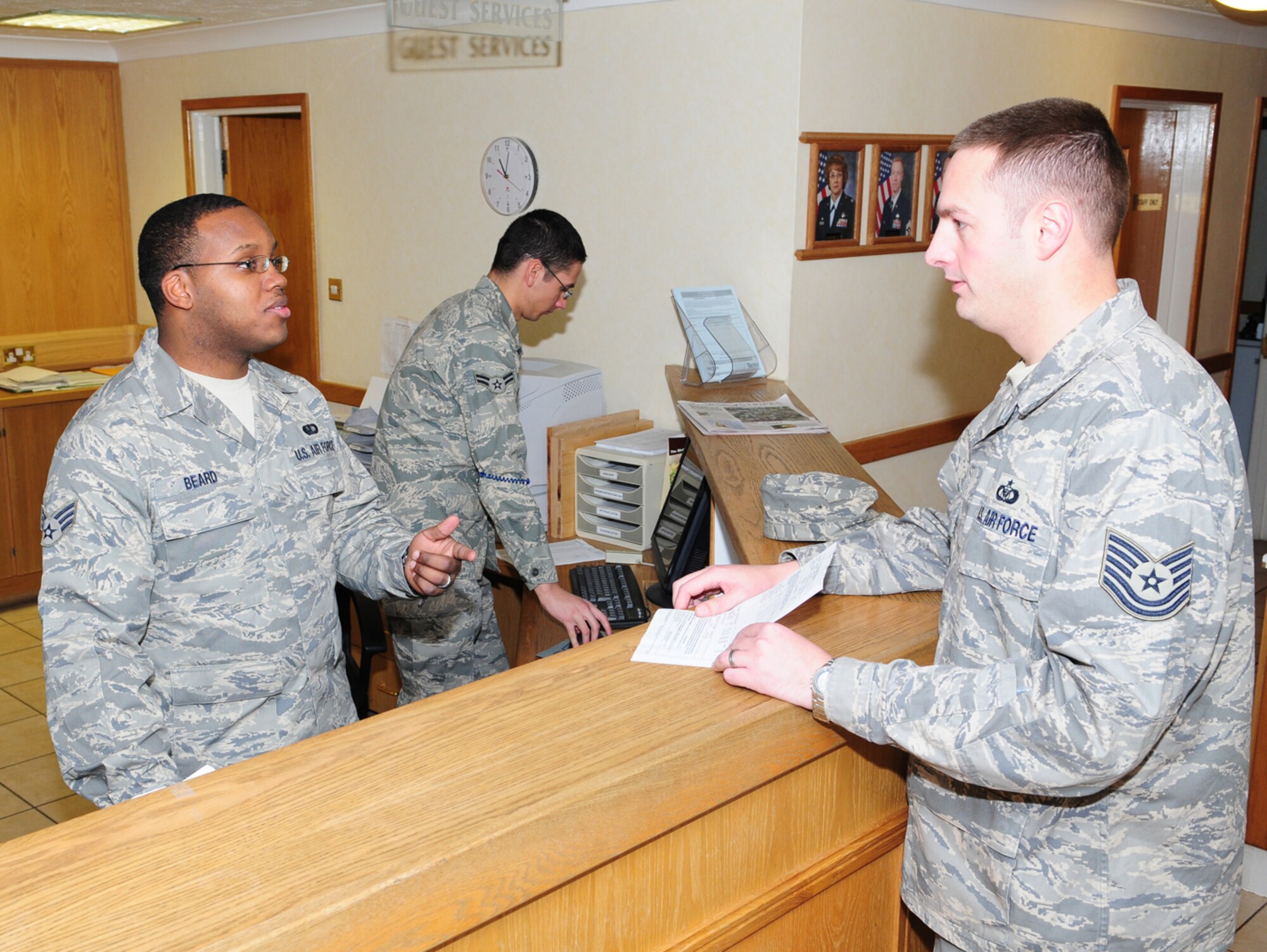 Senior Airman Marquette Beard, left, 100th Force Support Squadron Gateway Inn front desk clerk, talks with Tech. Sgt. Donald Allen, right, 727th Air Mobility Squadron, about the Prime Knight service Dec. 2, as Airman 1st Class Larry Mullikin,  also a front desk clerk, deals with other lodging issues. Sergeant Allen works with the Gateway Inn’s Prime Knight service to coordinate lodging for all transient aircrew, which helps reduce ground time by getting the aircrew in and out of lodging more quickly. About one-third of rooms are occupied by Air Mobility Command transient aircrew at any given time. After bringing the aircrew orders to the front desk staff, lodging makes up the room keys, which Sergeant Allen then collects and takes out to the aircraft. The keys are then given straight to the aircrew, which means they don’t then have to wait in line at lodging. Airman Beard said this process can save the aircrew between two and three hours ground time. (U.S. Air Force photo by Karen Abeyasekere)