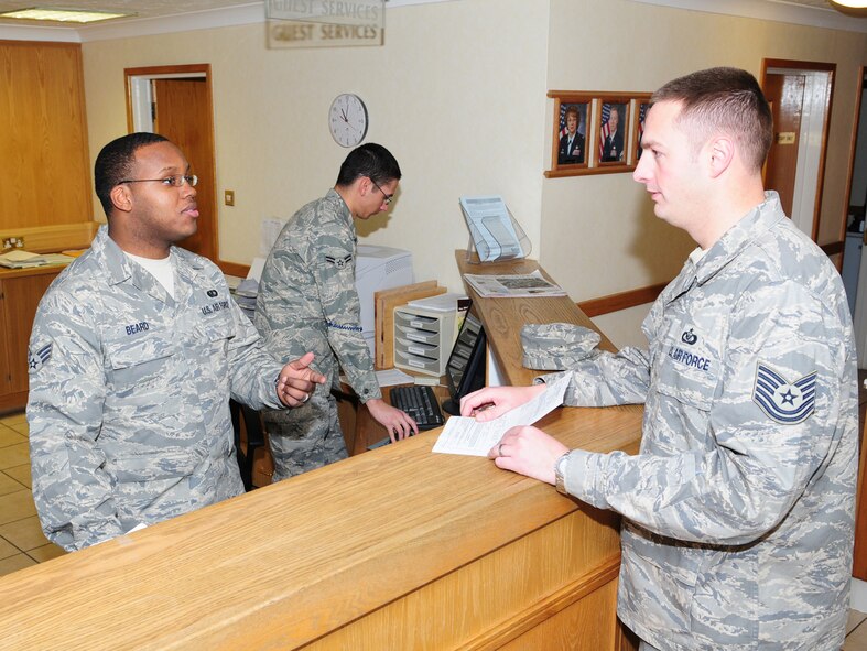 Senior Airman Marquette Beard, left, 100th Force Support Squadron Gateway Inn front desk clerk, talks with Tech. Sgt. Donald Allen, right, 727th Air Mobility Squadron, about the Prime Knight service Dec. 2, as Airman 1st Class Larry Mullikin,  also a front desk clerk, deals with other lodging issues. Sergeant Allen works with the Gateway Inn’s Prime Knight service to coordinate lodging for all transient aircrew, which helps reduce ground time by getting the aircrew in and out of lodging more quickly. About one-third of rooms are occupied by Air Mobility Command transient aircrew at any given time. After bringing the aircrew orders to the front desk staff, lodging makes up the room keys, which Sergeant Allen then collects and takes out to the aircraft. The keys are then given straight to the aircrew, which means they don’t then have to wait in line at lodging. Airman Beard said this process can save the aircrew between two and three hours ground time. (U.S. Air Force photo by Karen Abeyasekere)