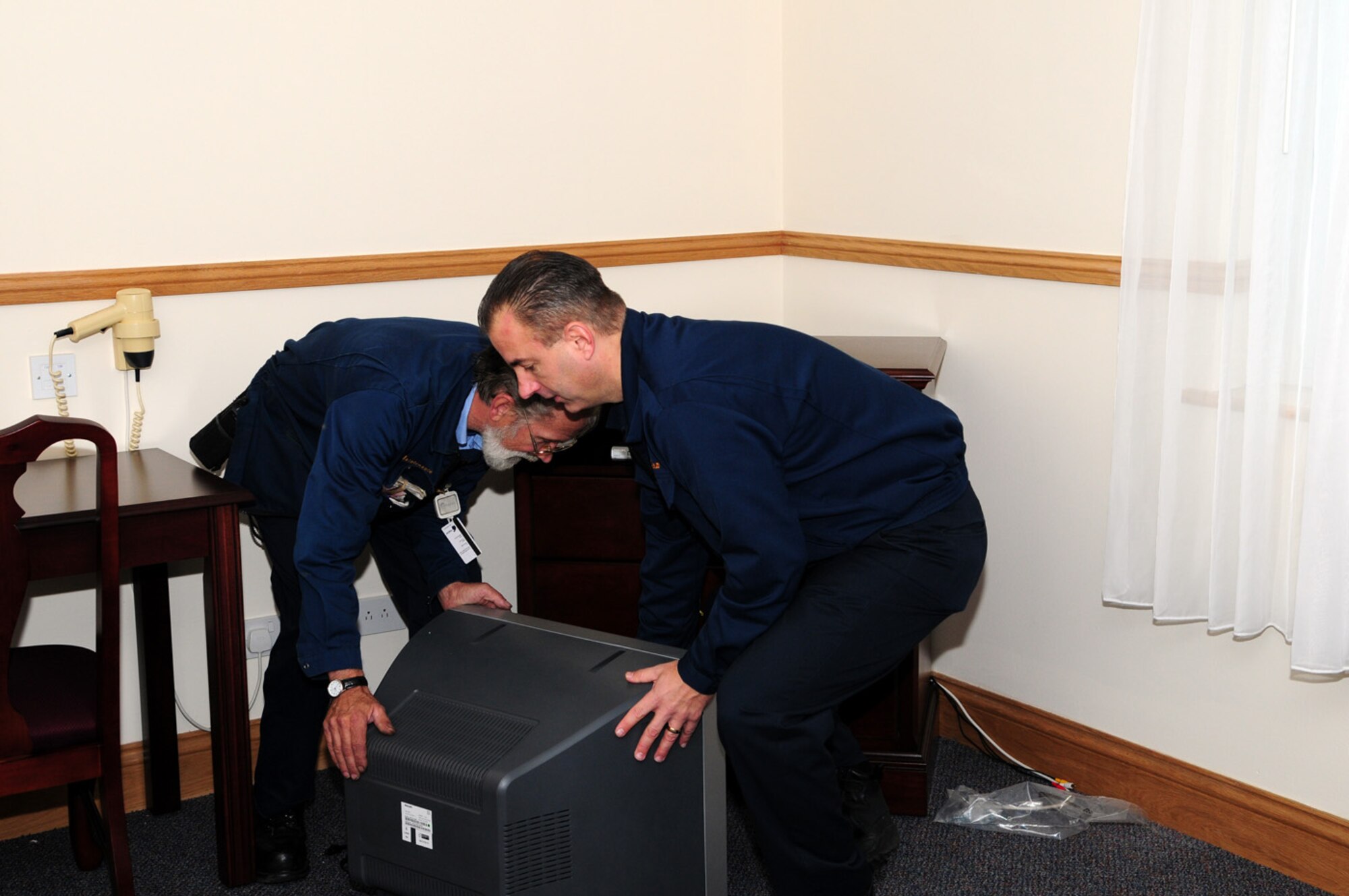 Dave Lawrence, right, 100th FSS Gateway Inn maintenance supervisor, helps David Beckett, maintenance worker, lift a television back onto its stand in one of the lodging rooms currently under renovation in Building 481. A whole-room renovation is in the final stages of the 48 guest rooms, corridors and lobby, which is an Air Force Services NAF project costing $466,000. Carpet is being replaced, as is all furniture, lamps and artwork, and there has also been window and wall treatments, including repainting. (U.S. Air Force photo by Karen Abeyasekere)