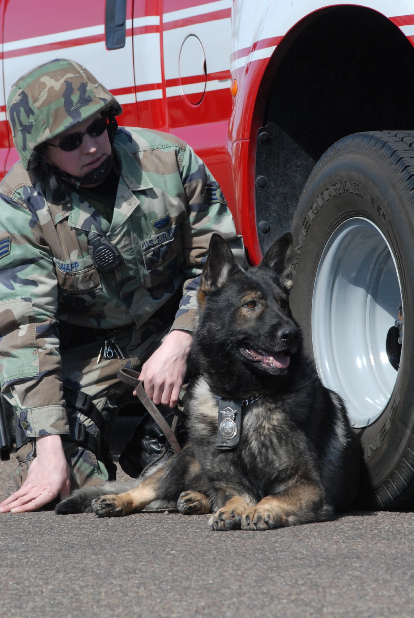 Senior Airman Caleb Snapp and his K-9 partner, Fritz, take cover beside a Malmstrom fire department vehiclewhile waiting for a call to assist during an exercise shooting scenario at the base clinic March 28. The duo is assigned to the 341st Security Forces Squadron. (U.S. Air Force photo/John Turner)