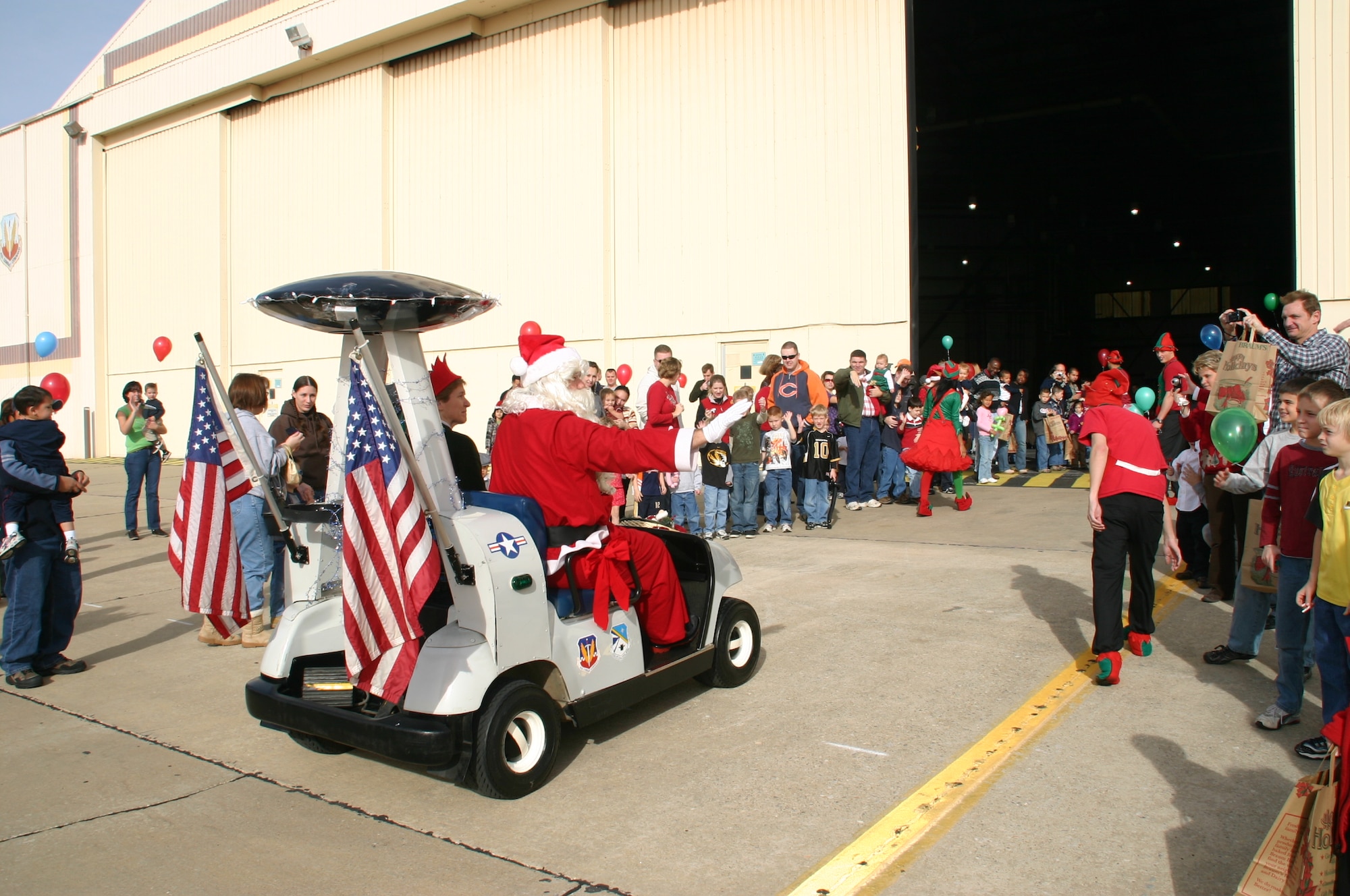 Santa Claus waves to the excited crowd of children and their parents as Col. Pat Hoffman, commander, 552 ACW chauffeurs him into the building in the AWACS golf cart. Photo courtesy of 1Lt Kinder Blacke.