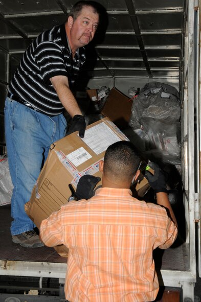SOUTHWEST ASIA -- Mike Ruzza off-loads the daily mail truck to Oneris Barett while he inspects the package for damage here Dec. 8. Mr. Ruzza and Mr. Barett work for Alutiiq International Solutions LCC. This company is contracted to provide personnel and services for the 380th Air Expeditionary Wing Post Office. They are busy trying to keep the mail coming and going during the busy holiday season. Mr. Ruzza is a native of Tampa Bay, Fla., and Mr. Barett is from Bronx, N.Y. (U.S. Air Force photo/Tech. Sgt. Christopher A. Campbell)(released)
