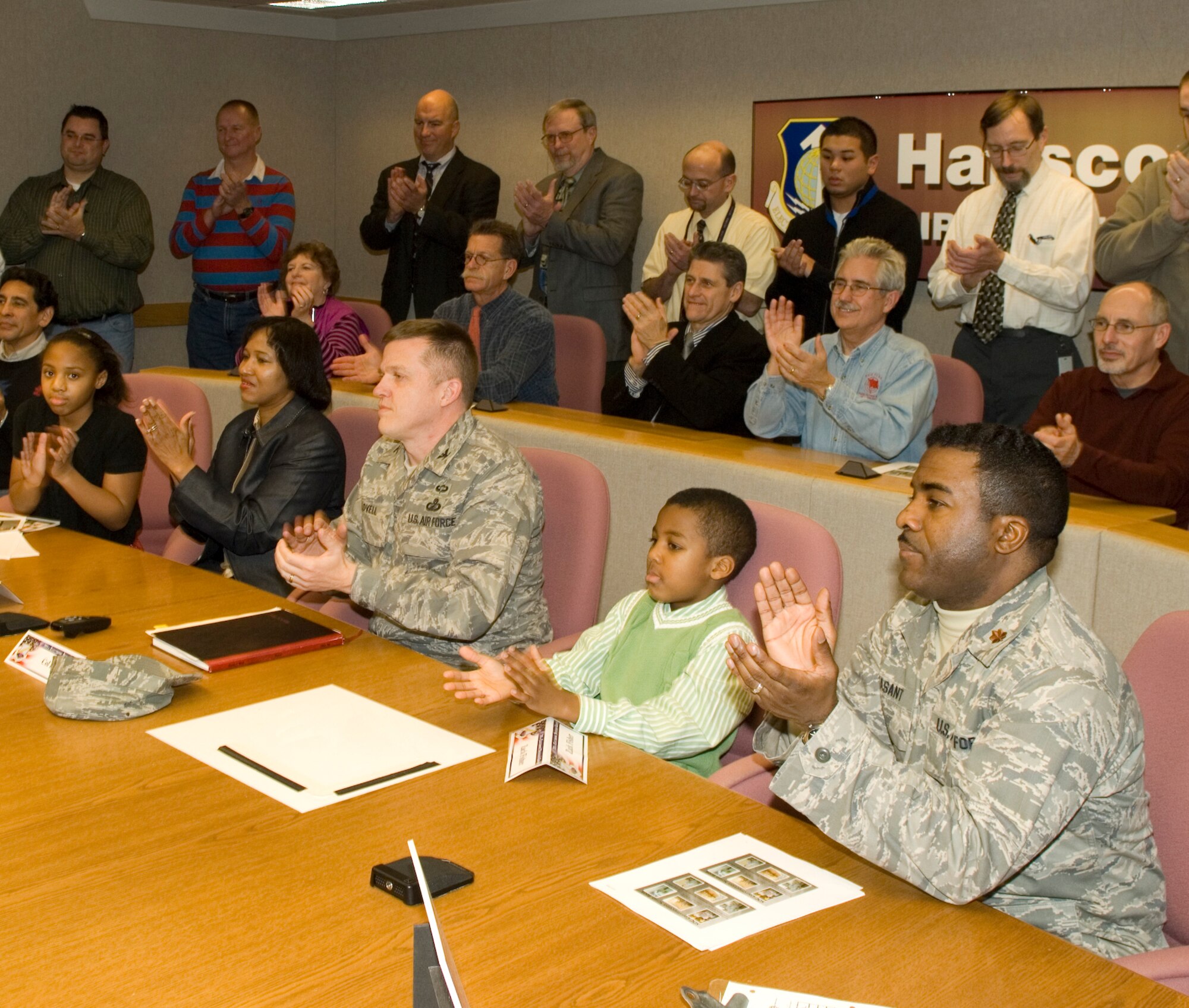 Family and coworkers of Lt. Col. Tyron Fisher, 632nd Electronic Systems Squadron commander, who has been deployed to Iraq for the past seven months, watch via video teleconference as he receives the Defense Meritorious Service Medal and the Iraqi Campaign Medal Dec. 5.  Looking on (front row from left) are daughter Tyra Fisher, wife Linda Fisher, 751st Electronic Systems Group Commander Col. Jim Lovell, son Zachary Fisher, Maj. George Peasant, as well as other members of the 751 ELSG.   (Photo by Rick Berry)