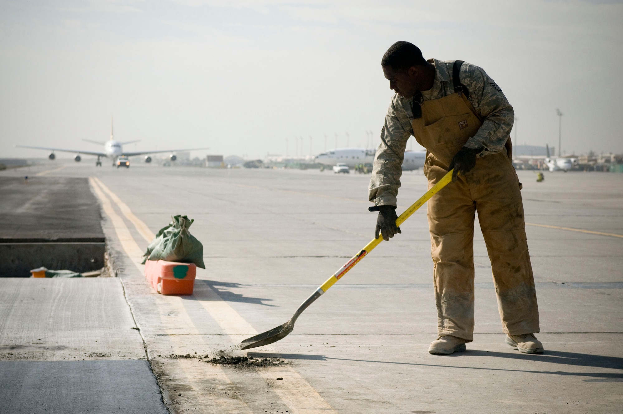 Staff Sgt. Shelton Jamison, 455th Expeditionary Civil Engineer Squadron, scoops away excess concrete on Thanksgiving Day, Nov. 27., at Bagram Air Field, Afghanistan. The Airmen of the 455th ECES must work quickly and efficiently to avoid causing traffic problems on the busy taxiway. Sgt. Jamison is deployed from Barksdale Air Force Base, La. (U.S. Air Force photo by Staff Sgt. Samuel Morse)(Released)