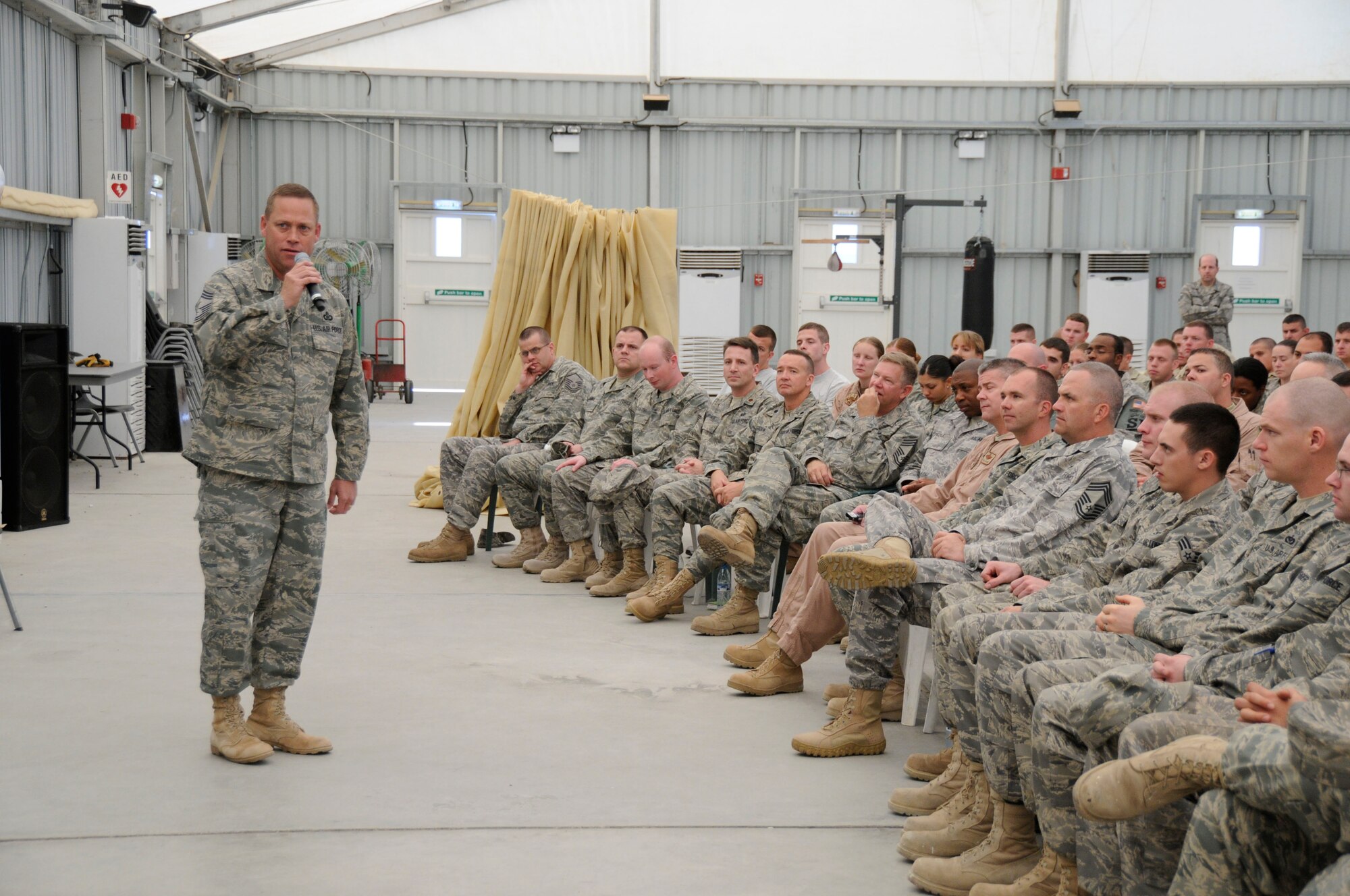 SOUTHWEST ASIA -- The 380th Air Expeditionary Wing Command Chief, Chief Master Sgt. Kent Smith, addresses a crowd of over 400 Airmen during the warfighter briefing here Dec. 10. The chief directed his comments toward the health and well-being of the Airmen as they near the close of their deployment. The briefing is intended to share highlights from the AEF rotation and remind Airmen to stay focused through the transition.  (US Air Force photo by Tech. Sgt. Christopher Campbell) (released) 
