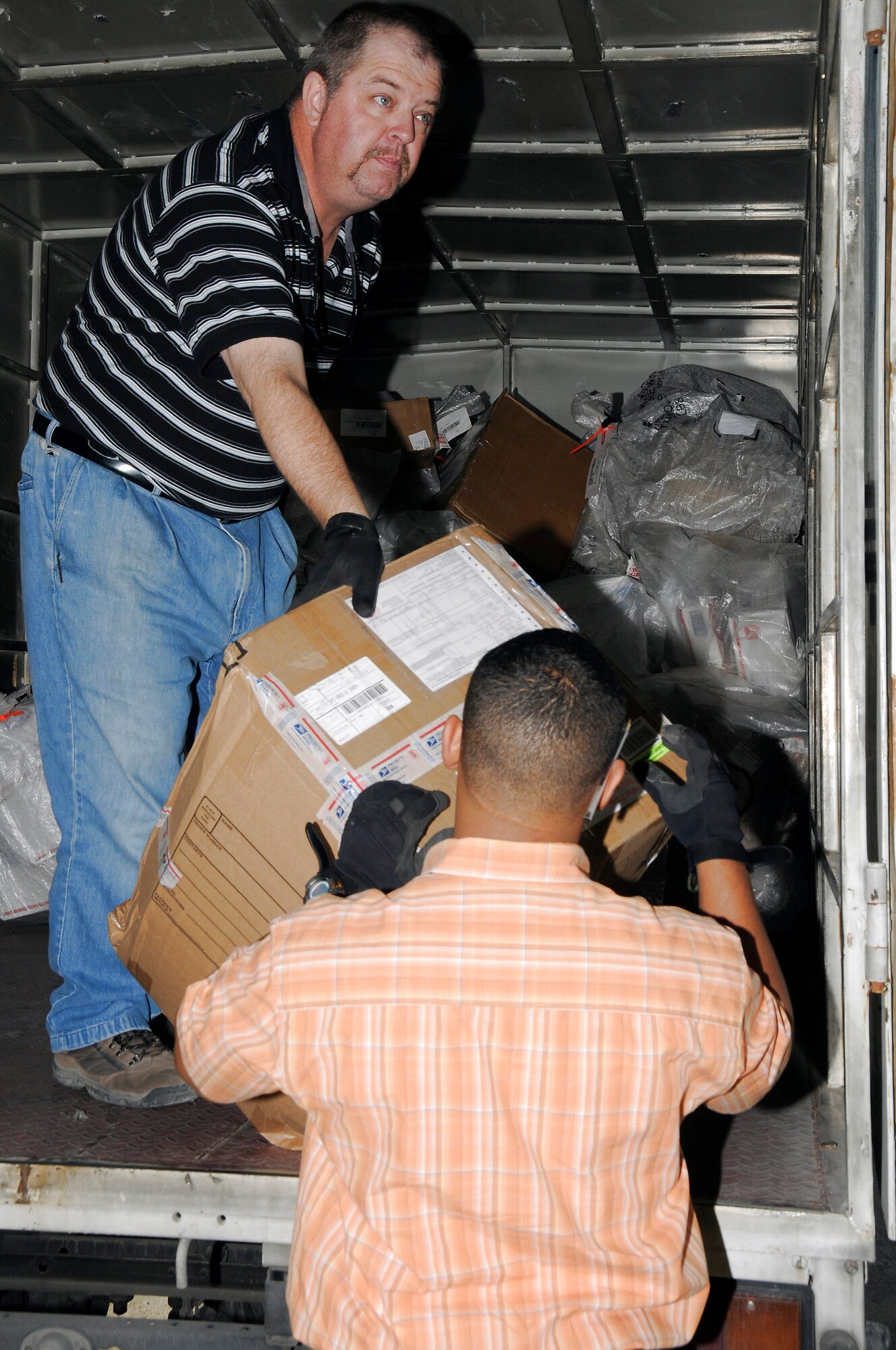 Mike Ruzza off loads the daily mail truck to Oneris Barett while he inspects the package for damage Dec. 8 at an air base in Southwest Asia. Mr. Ruzza and Mr. Barett work for Alutiiq International Solutions LCC. This company is contracted to provide personnel and services for the 380th Air Expeditionary Wing Post Office. They are busy trying to keep the mail coming and going during the busy holiday season. Mr. Ruzza is a native of Tampa Bay, Fla., and Mr. Barett is from the Bronx, N.Y. (U.S. Air Force photo/Tech. Sgt. Christopher A. Campbell) 
