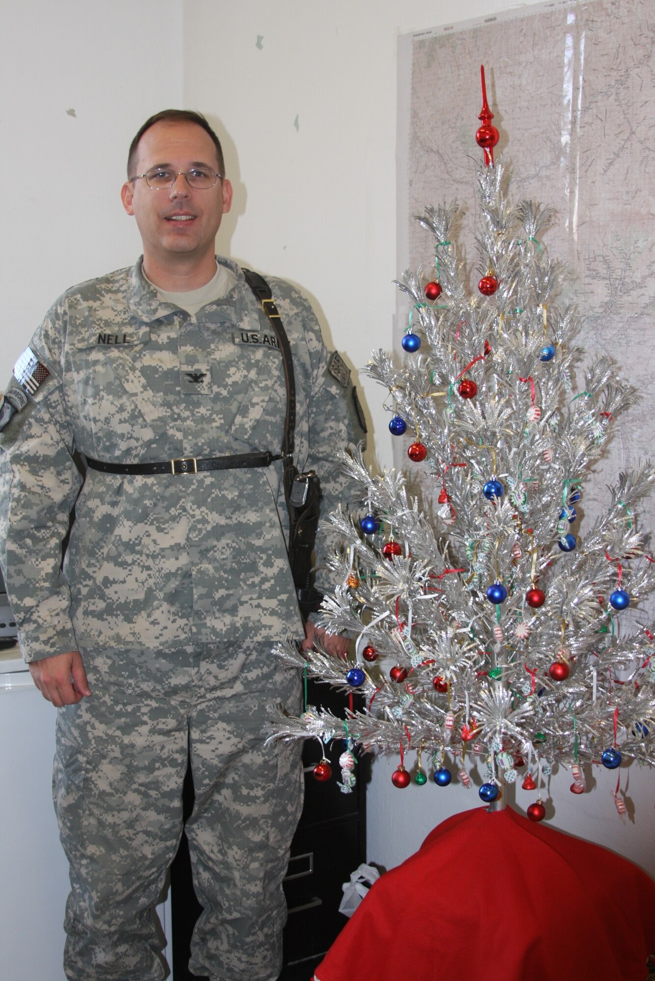 Colonel Roger Nell, command judge advocate at Task Force Warrior, stands in his office at Bagram Air Field, Afghanistan, Nov. 29 beside the artificial Christmas tree that holds over 40 years of service tradition in his family.  Purchased by his mother in the late 60s, the tree is now on its third wartime deployment, and sixth deployment overall.   
