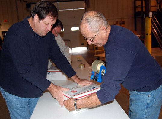 Kelly Helms and Al Maflin work together to tape up a care package during the final phase of Operation Happy Holidays Dec. 6. Mr. Helms is the Chief of Manpower and Organization for the 341st Force Support Squadron and Mr. Maflin is a retired senior master sergeant. (U.S. Air Force photo/Valerie Mullett)