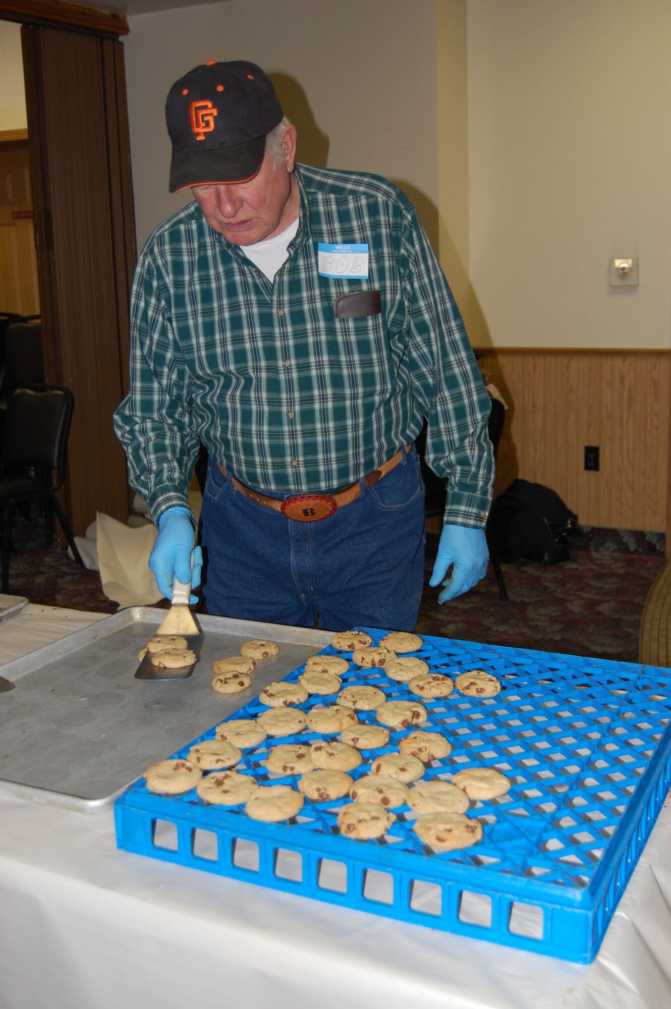 Bob Smith removes hot chocolate chip cookies onto a cooling rack during the first day of baking at the VFW Dec. 1. The group started at 6 a.m. and by 12:30 p.m., they had baked, cooled and packaged 292 dozen cookies. (U.S. Air Force photo/Valerie Mullett)
