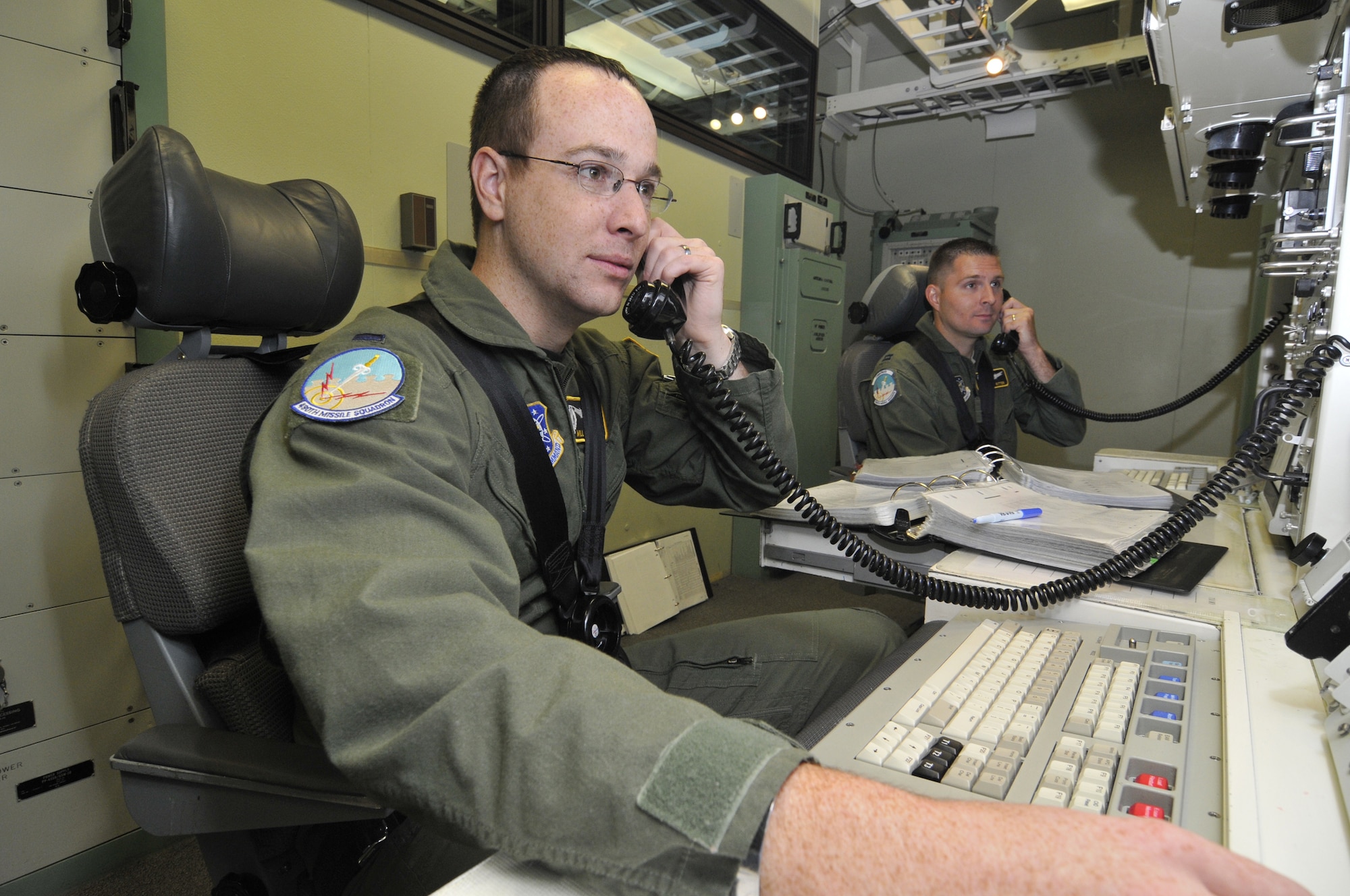 Capt. Jeremy Ritter, 490th Missile Squadron flight commander (right), and 1st Lt. William Springer, 490th MS ICBM combat crew deputy commander  (left), are "strapped in" and coordinating with the other launch crews to turn keys to launch their missiles during a simulation in the Missile Procedure Trainer. Crews "strap in" (buckle up) to prevent being thrown around the capsule in the event that they are attacked. (U.S. Air Force photo/John Turner)