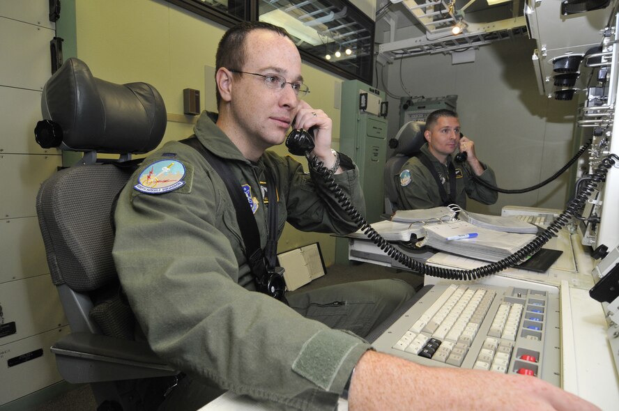 Capt. Jeremy Ritter, 490th Missile Squadron flight commander (right), and 1st Lt. William Springer, 490th MS ICBM combat crew deputy commander  (left), are "strapped in" and coordinating with the other launch crews to turn keys to launch their missiles during a simulation in the Missile Procedure Trainer. Crews "strap in" (buckle up) to prevent being thrown around the capsule in the event that they are attacked. (U.S. Air Force photo/John Turner)