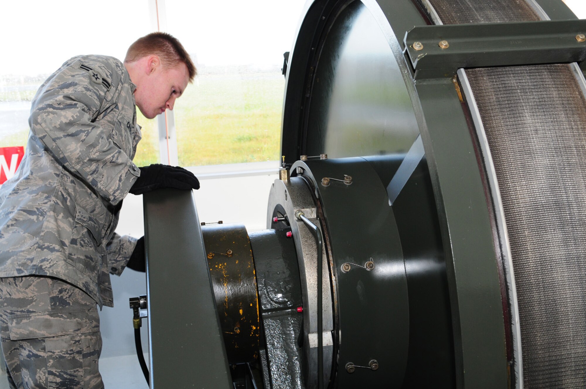 Airman 1st Class Andrew Cates, 100th CES Barrier Maintenance, performs a visual check on the equipment in one of the barrier shacks on the flightline. A giant reel of 7.75 inch-wide tape, with a maximum pull-out length of 1,200 feet, is part of the BAK-12 equipment in each of the shacks. The tape stretches from inside the shack, goes underground and exits on the side of the runway. There, it is connected to a cable which, when necessary during a barrier engagement, is stretched across the flightline and reconnects to another reel of tape which runs to another barrier shack on the opposite side. Barrier checks are performed daily. Technicians check the oil and perform daily maintenance, which includes checking hydraulic fluid and pressure, and deck sheaves for freedom of operation, to make sure everything is fully operational. The engine inside the shack is started up daily, and runs for about 10 minutes, during which time the engines inside the other shacks are started up and other checks done. During the journey to each shack, the cables are also checked to make sure there are no kinks, bends or tears. After the engine is run for 10 to 15 minutes, the power take-off is engaged, which connects the braking system to the engine. The purpose of the system is to save pilots lives and the aircraft, and works similar to brakes on a car by applying gradual pressure to the brakes, which brings the aircraft to a slow stop. Once the aircraft comes in and hooks onto the cable, it stops within a matter of seconds and within 1,200 feet. (U.S. Air Force photo by Karen Abeyasekere)