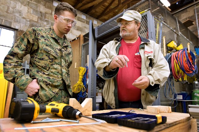 A.C. Strickland, troop training and self-help supervisor for Public Work's Self-Help Program, shows Cpl. Patrick Kelly, a training clerk, Headquarters Company, Marine Special Operations Group, Marine Special Operations Command, how to drill and mount brackets for curtains he is installing in his units conference room.