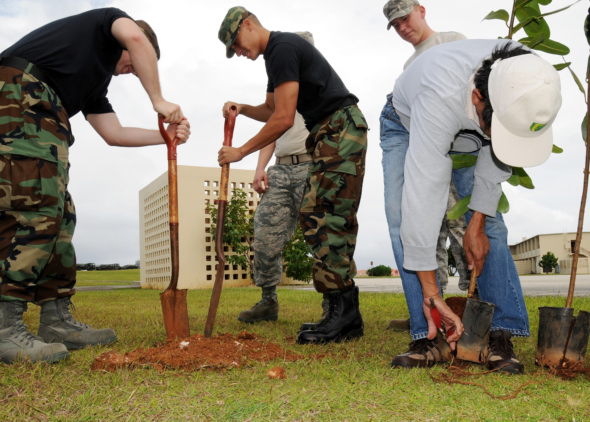 ANDERSEN AIR FORCE BASE, Guam -Airman Justin Scott (left) and Airman Dion Battisti (right) both 36th Civil Engineer Squadron Firefighters dig a hole measuring one foot deep while Mr. Tedy Magno 36th CES Ground Maintenance cuts the excess roots of the tree in preparation for planting at the First Term Airmen's Center here Dec. 11. This is the first Going Green project ever conducted by FTAC Airmen. (U.S. Air Force photo by Senior Airman Nichelle Griffiths)