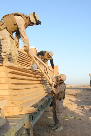 Marines with General Support Platoon, Company B, 1st Combat Engineer Battalion, Regimental Combat Team 5 unload pre-fabricated rafter forms from the back of a trailer near the city of Haqlaniyah, Iraq, Dec 14. The engineers spent two days building wooden huts for the Iraqi Security Forces to stay in while they man a new Traffic Control Point. ::r::::n::