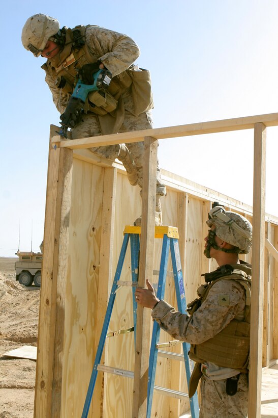 Cpl. Emilio Avalos, 20, from El Paso, Texas, shaves the edge off a brace that holds the newly erected wooden hut wall in place while Lance Cpl. Benjamin I. Cook, 19, from North Vernon, Ind., steadies the ladder.  Both Marines are combat engineers with General Support Platoon, Company B, 1st Combat Engineer Battalion, Regimental Combat Team 5. The engineers built the wooden hut near the city of Haqlaniyah, Iraq, Dec 14, to benefit the Iraqi Security Forces who will be living in them while manning the nearby Traffic Control Point. ::r::::n::