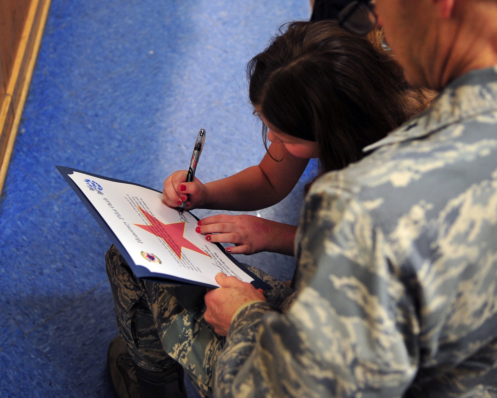Brig. Gen. Mark Graper, 354th Fighter Wing commander, watches as honorary 3rd Lt., Daphny Dunn signs her commission to the 18th Aggressor Squadron. Daphny and her family were visiting Eielson Air Force Base with the Make-A-Wish Foundation; Daphny came to the foundation while she was battling Leukemia. (U.S. Air Force photo/Airman 1st Class Willard E. Grande II)