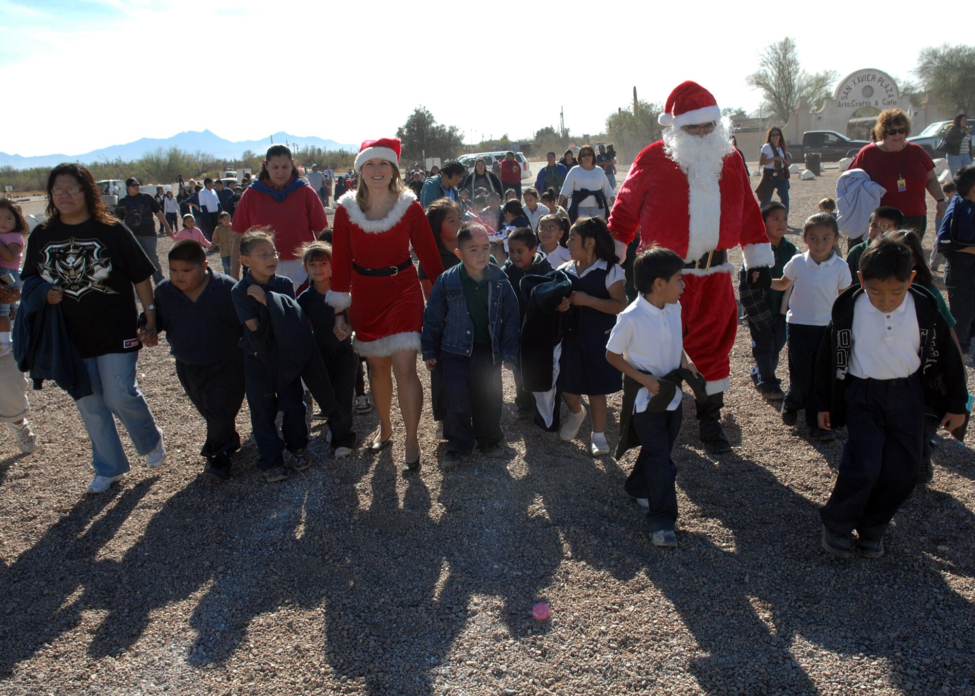 Santa and Mrs. Claus walk with students from St. Xavier Mission School after arriving in an HH-60 Pavehawk helicopter Dec. 15.  Mr. and Mrs. Claus were at the school to host the Santas in Blue event in which Airmen from D-M come together to give gifts to children for Christmas. The St. Xavier Mission School goes from kindergarten to eighth grade.  (U.S. Air Force Photo/Senior Airman Jacqueline Romero)  