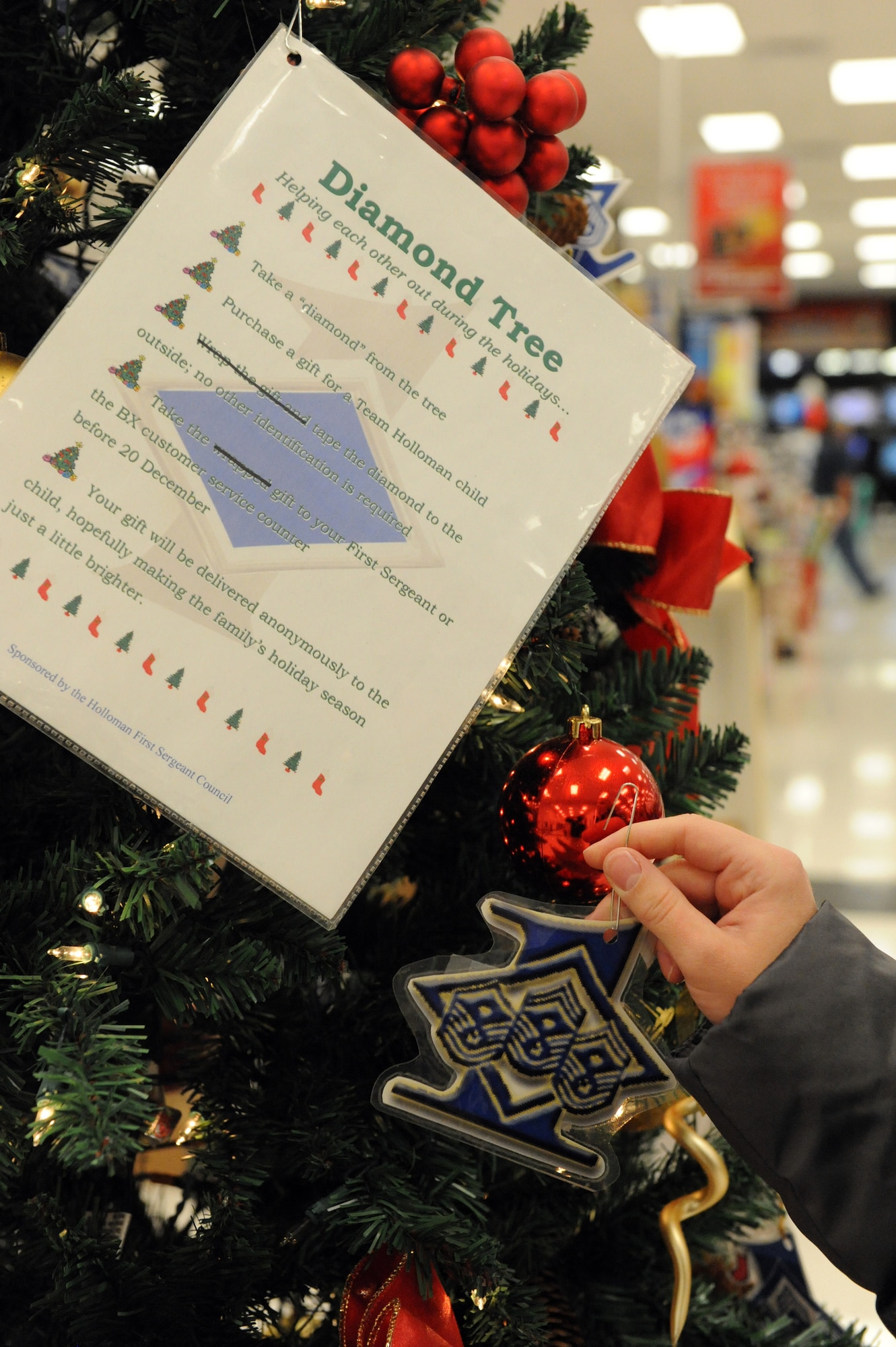 Airman Kimberly Hund, 49th Maintenance Operations Squadron, picks a name off of the Diamond Tree in the front entrance of the Base Exchange at Holloman Air Force Base, N.M., Dec. 11. The Diamond Tree is sponsored by the Holloman First Sergeant Council and is designed to help less fortunate Team Holloman families during the holiday season. Each diamond on the tree has information about a child. When a person picks that diamond, they buy them a gift and bring it to their first sergeant or the BX customer service counter. (U.S. Air Force photo/Airman 1st Class Sondra M. Escutia)