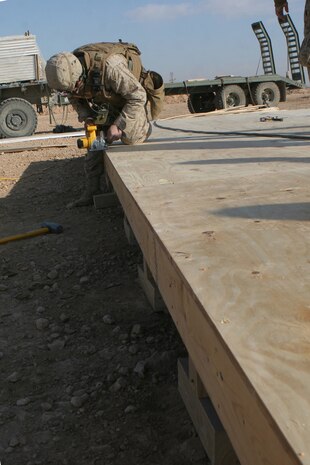 Staff Sgt. Andrew J. Cordova, 30, from Clovis, N.M., the platoon commander for General Support Platoon, Company B, 1st Combat Engineer Battalion, Regimental Combat Team 5, shaves off the edge of plywood flooring he and his fellow engineers have put in near Haditha, Iraq, Dec 15. The floor is the first step in the construction of a wooden hut being built for Iraqi Security Forces. The major pieces of the hut come pre-formed, but it still requires the skills and ingenuity of the engineers to piece them together.::r::::n::