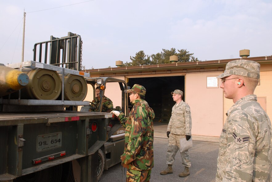 KUNSAN AIR BASE, Republic of Korea -- Airman 1st Class Thomas Williams and Staff Sgt. Christopher Noya, 8th Maintenance Squadron, observe as Republic of Korea Air Force Airman 1st Class Jin Seok Kim and Staff Sgt. Jong Mun Park load MK-84 general purpose bombs onto a 10 ton tractor trailer here Dec. 17. USAF and ROKAY Airmen work and train together regularly at Kunsan.(U.S. Air Force photo by: Senior Airman Angela Ruiz)
