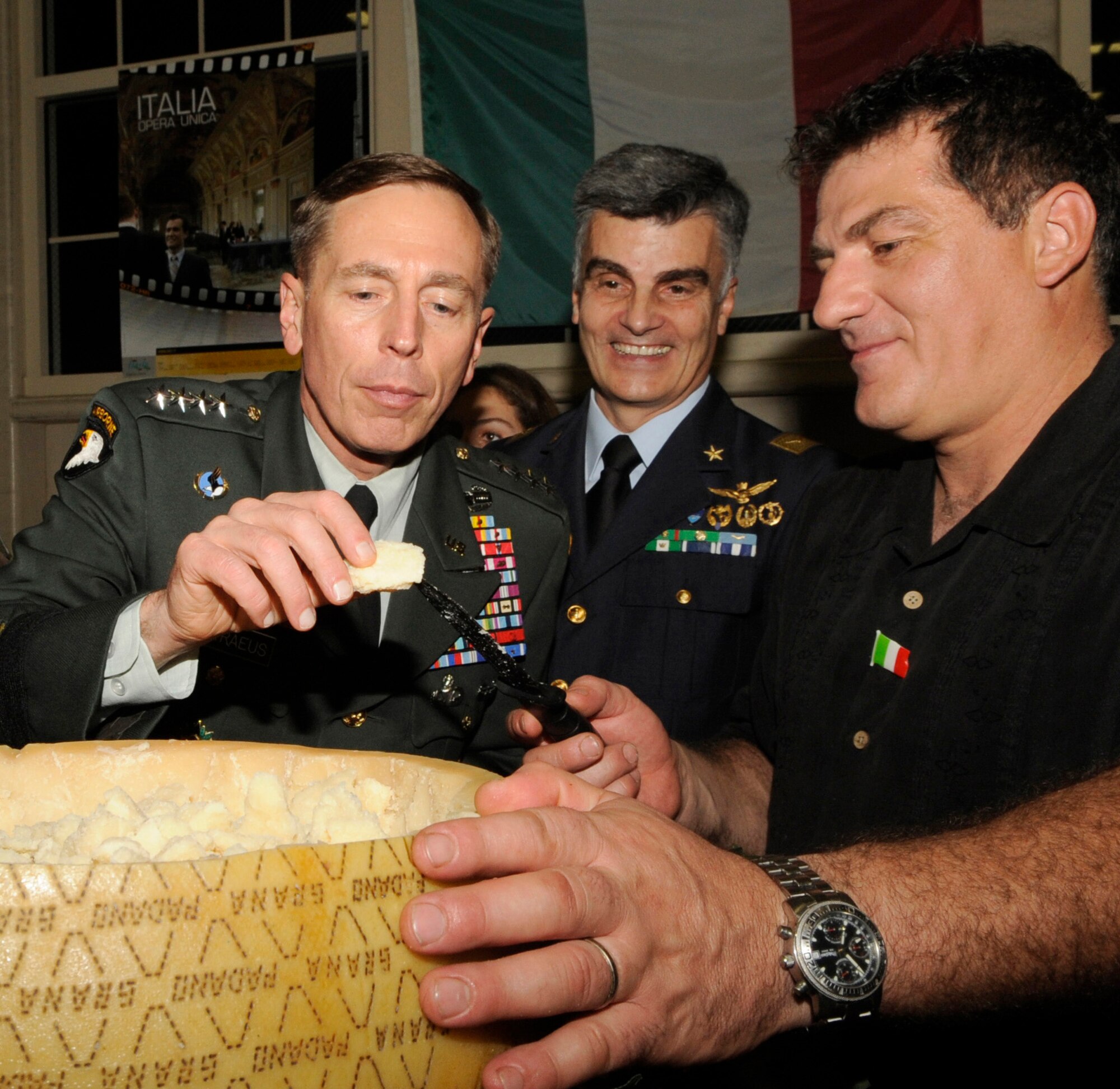 Gen. David Petraeus, United States Central Command commander, samples a piece of the legendary Parmigiano-Reggiano while Luigi and Brig. Gen. Enrico P. Bassignano, the Italian Senior Representative from CENTCOM, stand by to watch during the Coalition International Night held here in Hangar 1, Dec. 16. This year’s event marks the 5th anniversary of the annual tradition that allows military members and families to become more familiar with various native cuisines, customs and dress of the 63 different countries represented in the U.S. Central Command Coalition Village. During this event many Coalition members and their families volunteered to cook some of their countries favorite or famous cuisines to share. The event ended with the United States Central Command commander, Gen. David Petraeus, giving a thank you speech to all those who came out.