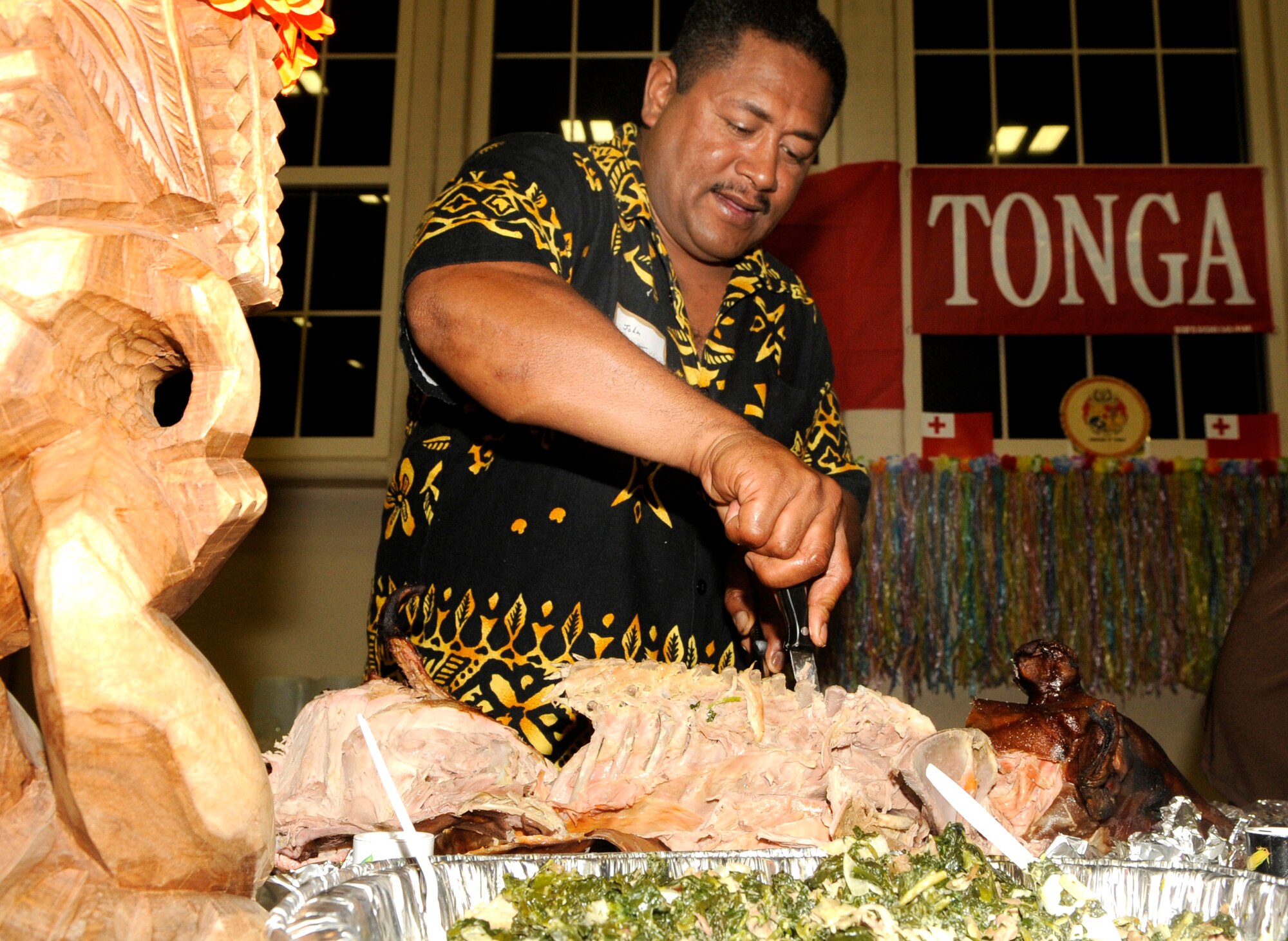 John Maafu from Kingdom of Tonga slices a whole roasted pig to serve during Coalition International Night held here in Hangar 1, Dec. 16. This year’s event marks the 5th anniversary of the annual tradition that allows military members and families to become more familiar with various native cuisines, customs and dress of the 63 different countries represented in the U.S. Central Command Coalition Village. During this event many Coalition members and their families volunteered to cook some of their countries favorite or famous cuisines to share. The event ended with the United States Central Command commander, Gen. David Petraeus, giving a thank you speech to all those who came out. The Kingdom of Tonga is in the South Pacific Ocean and consists of 71 islands, 48 of them inhabited.  The islands lie south of Samoa, about one-third of the way from New Zealand to Hawaii.