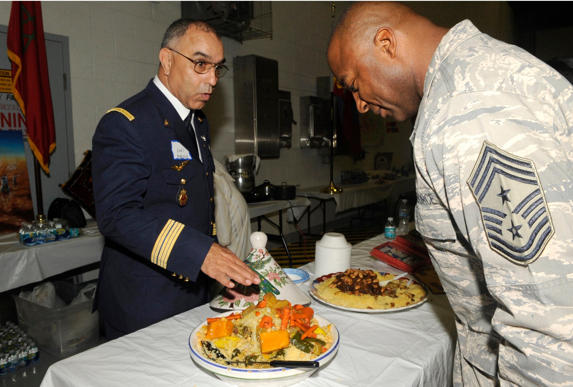 Col. Sori Nestaha from Morocco, offers a sample of couscous, or in Morocco, kuskus to Chief Master Sgt. Derrick Crowley, 6th Air Mobility Wing command chief during Coalition International Night held here Dec. 16 in Hangar 1. This year’s event marks the 5th anniversary of the annual tradition that allows military members and families to become more familiar with various native cuisines, customs and dress of the 63 different countries represented in the U.S. Central Command Coalition Village. During this event many Coalition members and their families volunteered to cook some of their countries favorite or famous cuisines to share. The event ended with the United States Central Command commander, Gen. David Petraeus, giving a thank you speech to all those who came out. 