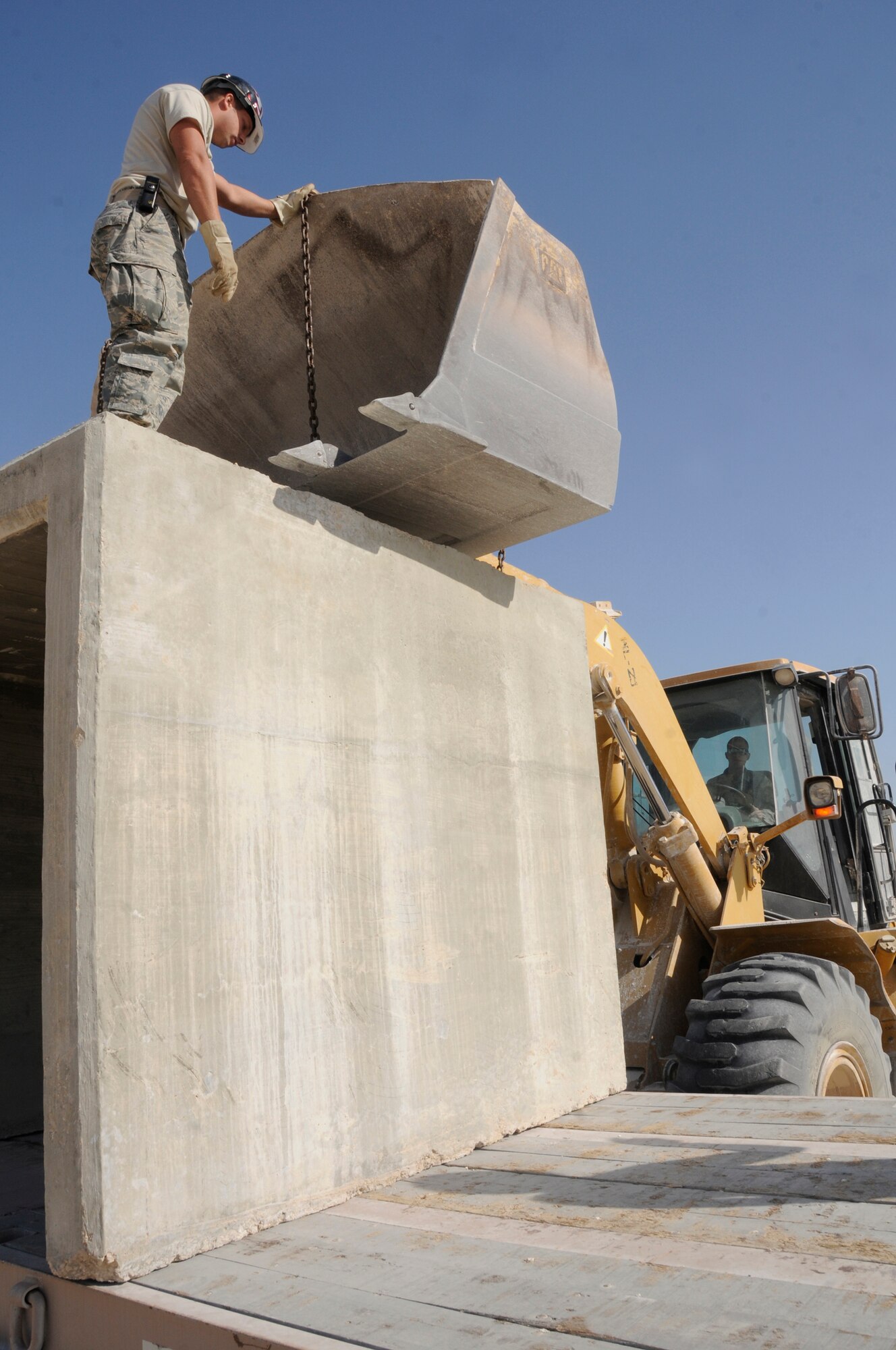 Staff Sgt. Chad Roberts chains a barrier to a front-end loader controlled by Airman 1st Class Ryan Miller Dec. 16, at an undisclosed air base in Southwest Asia.  The barriers will be loaded on a flat-bed truck for transportation to the ECES compound where they will be used to construct an emergency bunker.  Both Airmen are pavements maintenance technicians assigned to the 379th Expeditionary Civil Engineer Squadron.  Sergeant Roberts, a native of Lancaster, Ohio, is deployed from Scott Air Force Base, Ill.  Airman Miller, a native of Tulsa, Okla., is deployed from Grand Forks AFB, N.D. Both are deployed in support of Operations Iraqi and Enduring Freedom and Joint Task Force-Horn of Africa. (U.S. Air Force photo by Staff Sgt. Darnell T. Cannady/Released)