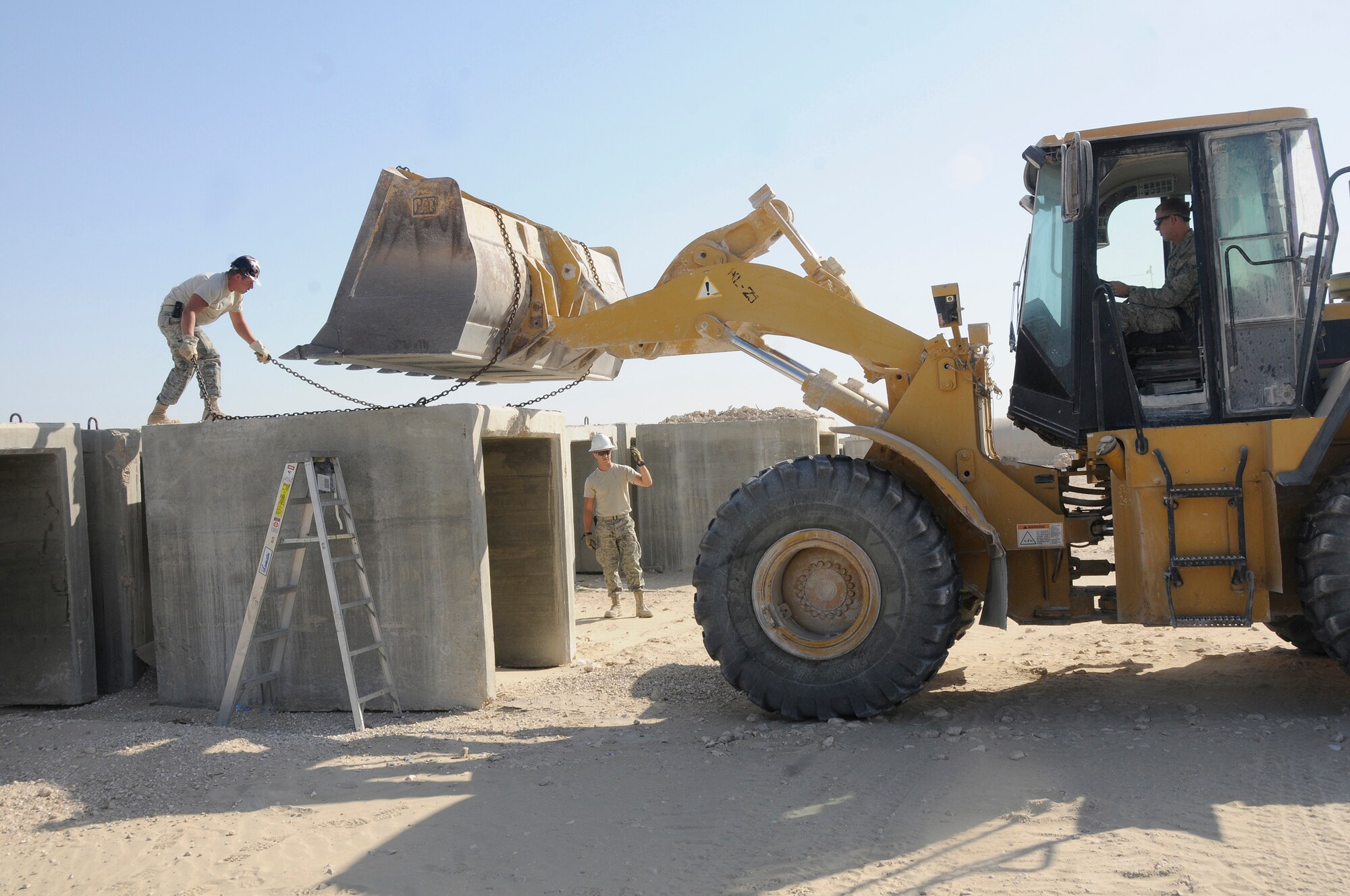 Staff Sgt. Chad Roberts chains a barrier while Airman 1st Class Andrew Sanders directs a front-end loader controlled by Airman 1st Class Ryan Miller Dec. 16, at an undisclosed air base in Southwest Asia.  The barriers will be loaded on a flat-bed truck for transportation to the ECES compound where they will be used to construct an emergency bunker.  All three Airmen are pavements maintenance technicians assigned to the 379th Expeditionary Civil Engineer Squadron.  Sergeant Roberts, a native of Lancaster, Ohio, is deployed from Scott Air Force Base, Ill.  Airman Sanders, a native of Payson, Ariz., is deployed from Spangdahlem Air Base, Germany. Airman Miller, a native of Tulsa, Okla., is deployed from Grand Forks AFB, N.D. All are deployed in support of Operations Iraqi and Enduring Freedom and Joint Task Force-Horn of Africa. (U.S. Air Force photo by Staff Sgt. Darnell T. Cannady/Released)