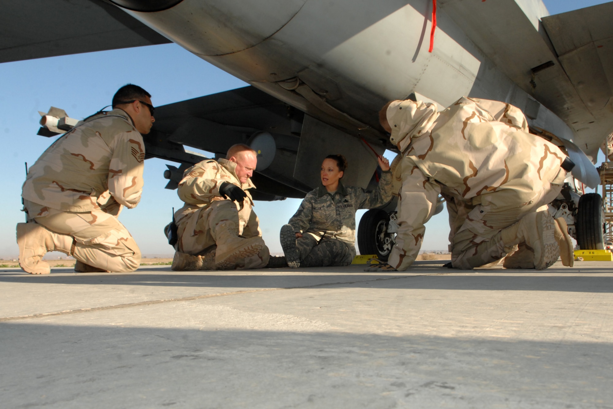 Master Sgt. Renee Miller explains the arresting hook, on the underside of an F-16, to Staff Sgt. Frank Martinez(left), Master Sgt. Braxton Simmons(center), and Senior Airman Trent Buzille(right), during egress training at Kirkuk Regional Air Base, Iraq, Dec. 16. The training provided the firefighters hands-on familiarization with the jet in case of an emergency requiring egress.  The firefighters are part of the 506th Expeditionary Civil Engineering Squadron.  Sergeant Miller is the transient alert flight chief with the 506th Expeditionary Operations Support Squadron and is deployed from Luke Air Force Base, Ariz. All three firefighters are deployed from Charleston AFB, S.C. (U.S. Air Force photo/Senior Airman Randi Flaugh)