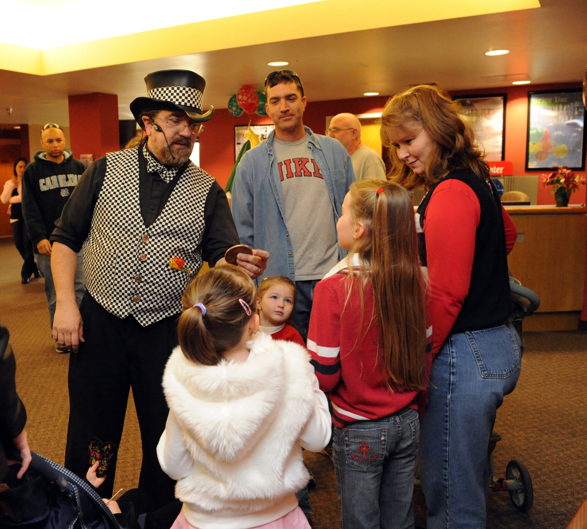 Mr. Jamie O'Hara, the Magic Guy, performs a magic trick with a coin to a family attending the International Children's Festival at the Community Center at Holloman Air Force Base, N.M., Dec. 13. The festival was created to give children a look at diverse Air Force families and their holiday traditions.  More than 650 people attended. (U.S. Air Force photo/Airman 1st Class Sondra Escutia)