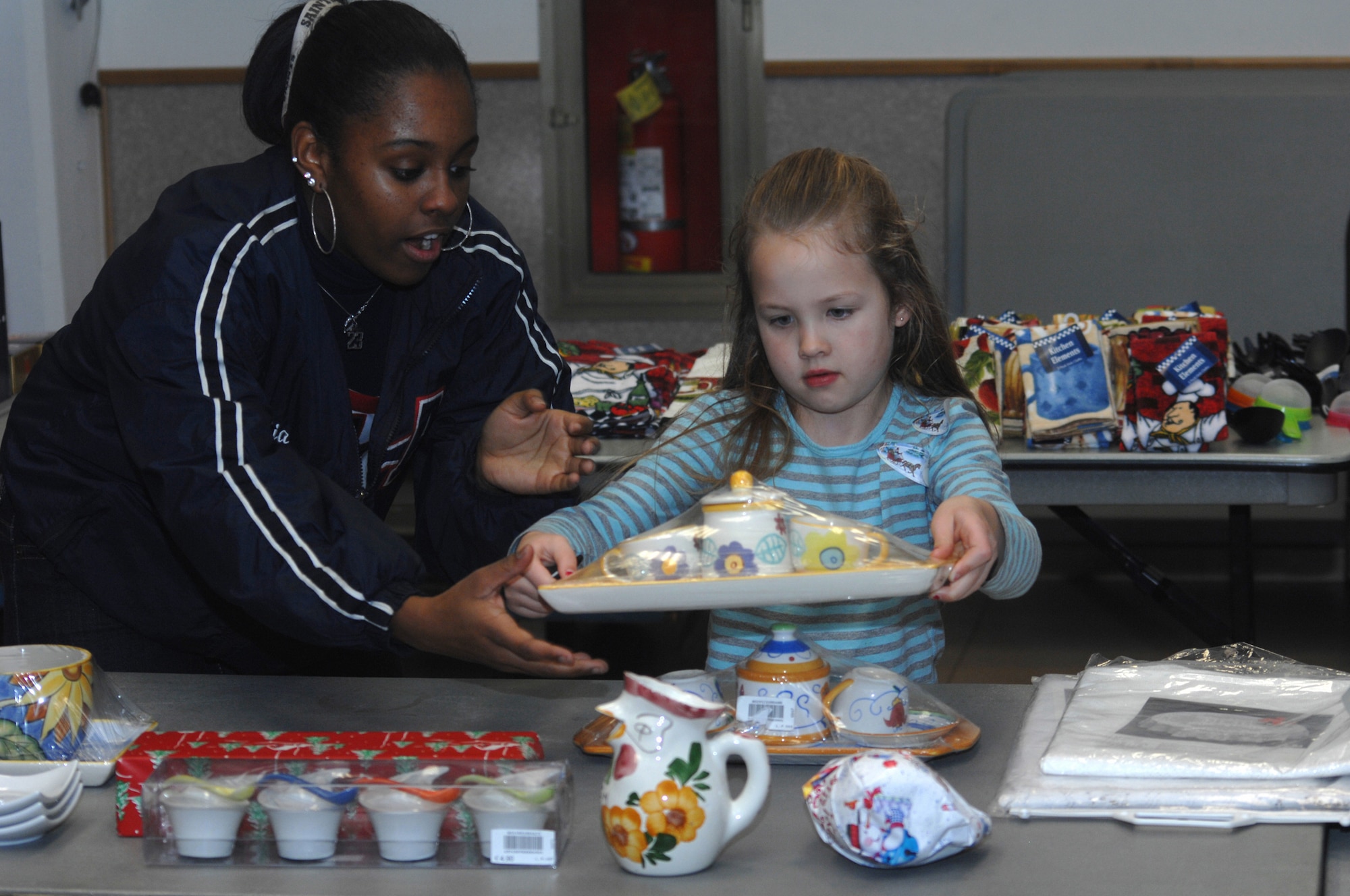 Aviano High School cheerleader Kia Patterson helps Emma Kluver, daughter of Staff Sgt. Ryan and Donna Kluver, with a gift for her mom during the Aviano Officers and Civilians Spouses Club annual Christmas Cottage Dec. 16 at the Community Center. The cottage, hosted by the AOCSC, allows children to pick out a gift, wrap it and give it to their parents for Christmas. Aviano High School Cheerleaders and AOCSC volunteers helped the children pick out presents and wrap them. (U.S. Air Force photo/Senior Airman Justin Weaver)