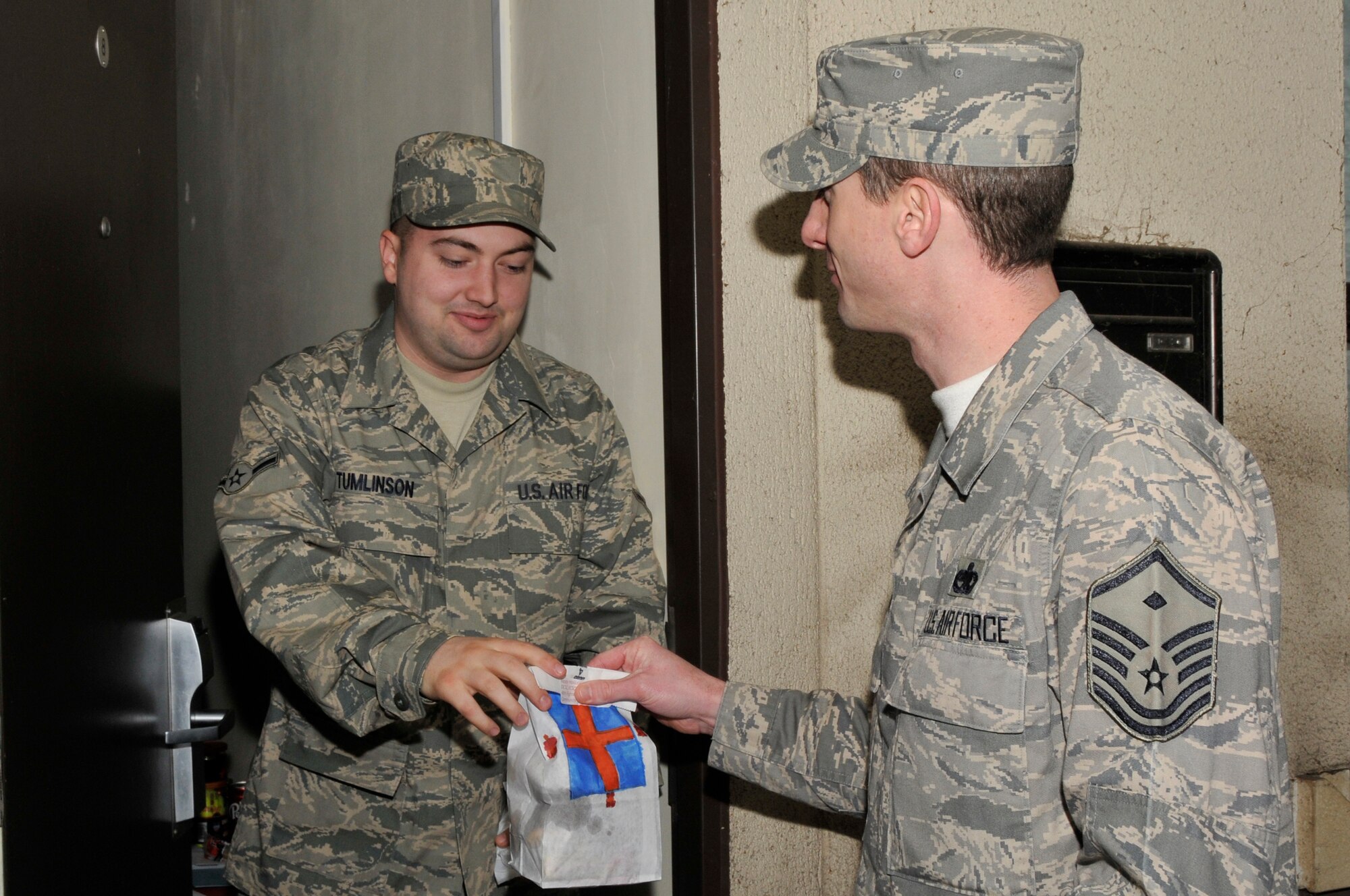 Master Sgt. Michael Sanders, 56th Rescue Squadron First Sergeant, delivers a bag of donated cookies to Airman Joshua Tumlinson, 48th Operation Support Squadron Dec. 12 at RAF Lakenheath, England. First Sergeants spent the day delivering bags of donated cookies to single Airman living in the dormitories. (U.S. Air Force photo by Airman 1st Class Perry Aston)