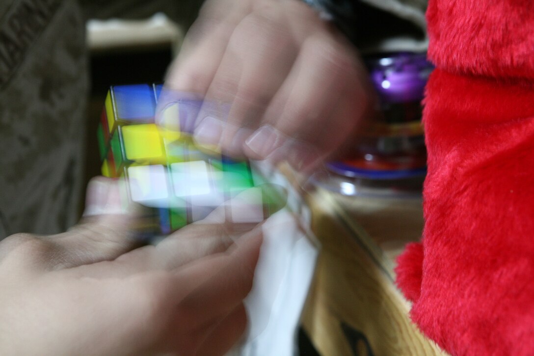 Lance Cpl. Michael Dunn, mail clerk with Regimental Combat Team 5, takes time out from sorting packages at Camp Ripper Iraq, Dec. 20, to try and solve a Rubik's Cube, one gift that filled out a stocking sent to Marines and sailors of RCT-5. Games, socks, hygiene items and holiday snack are found in stockings and care packages distributed to the troops deployed to the Middle East.::r::::n::