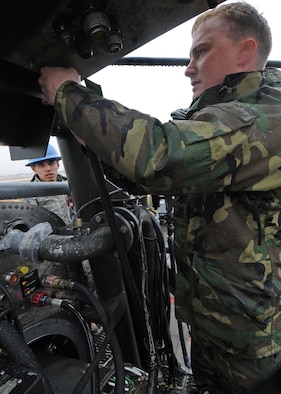 YOKOTA AIR BASE, Japan -- Airman 1st Class Jorge Espinosa-Velez watches Senior Airman Mathew Vineyard  prepare to attach hydraulic plugs to the back of a T56 engine Dec. 17. The plugs are attached just before the engine is tested for routine maintenance.  The Airmen work for the 374th Maintenance Squadron engine test cell. (U.S. Air Force photo by Senior Airman Veronica Pierce)
