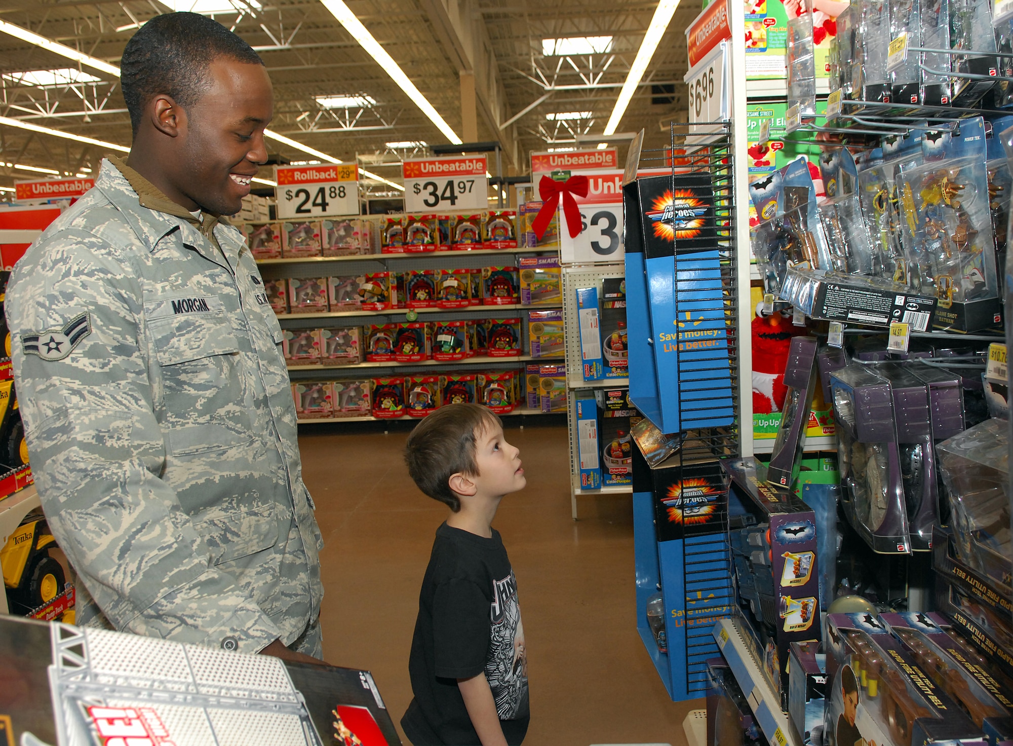 MINOT, N.D. -- Airman 1st Class Kenny Morgan, 5th Security Forces Squadron, smiles while Riley Wesley, a kindergartener at Washington Elementary School, tries to decide which toy to purchase during the 6th annual Shop with a Cop at Walmart here Dec 21. Children participated in four activities throughout the year in the Companions for Children program to earn the shopping spree. This year 52 children each received $150 in gift cards to buy gifts for themselves or family members. (U.S. Air Force photo by Tech. Sgt. Linda Miller)