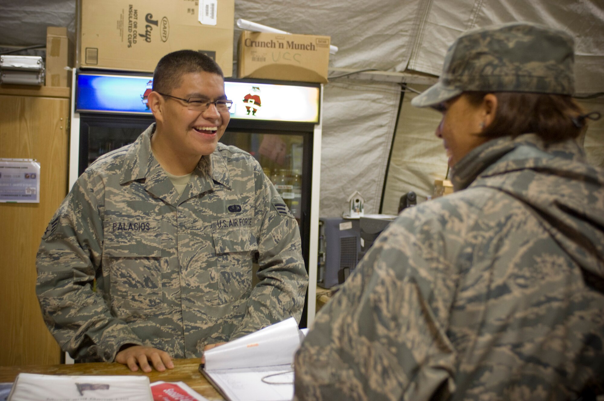 Senior Airman Marco Palacios, 455th Expeditionary Force Support Squadron services technician, helps a customer in the services tent at Bagram Air Field, Afghanistan, Dec. 17. Airman Palacios, deployed from Beale Air Force Base, Calif., made an effort to improve morale for deployed Airmen over the holidays by taping readings of ?A Night Before Christmas,? and creating e-cards of Airmen?s picture with Santa. (U.S. Air Force photo by Staff Sgt. Rachel Martinez)(Released)