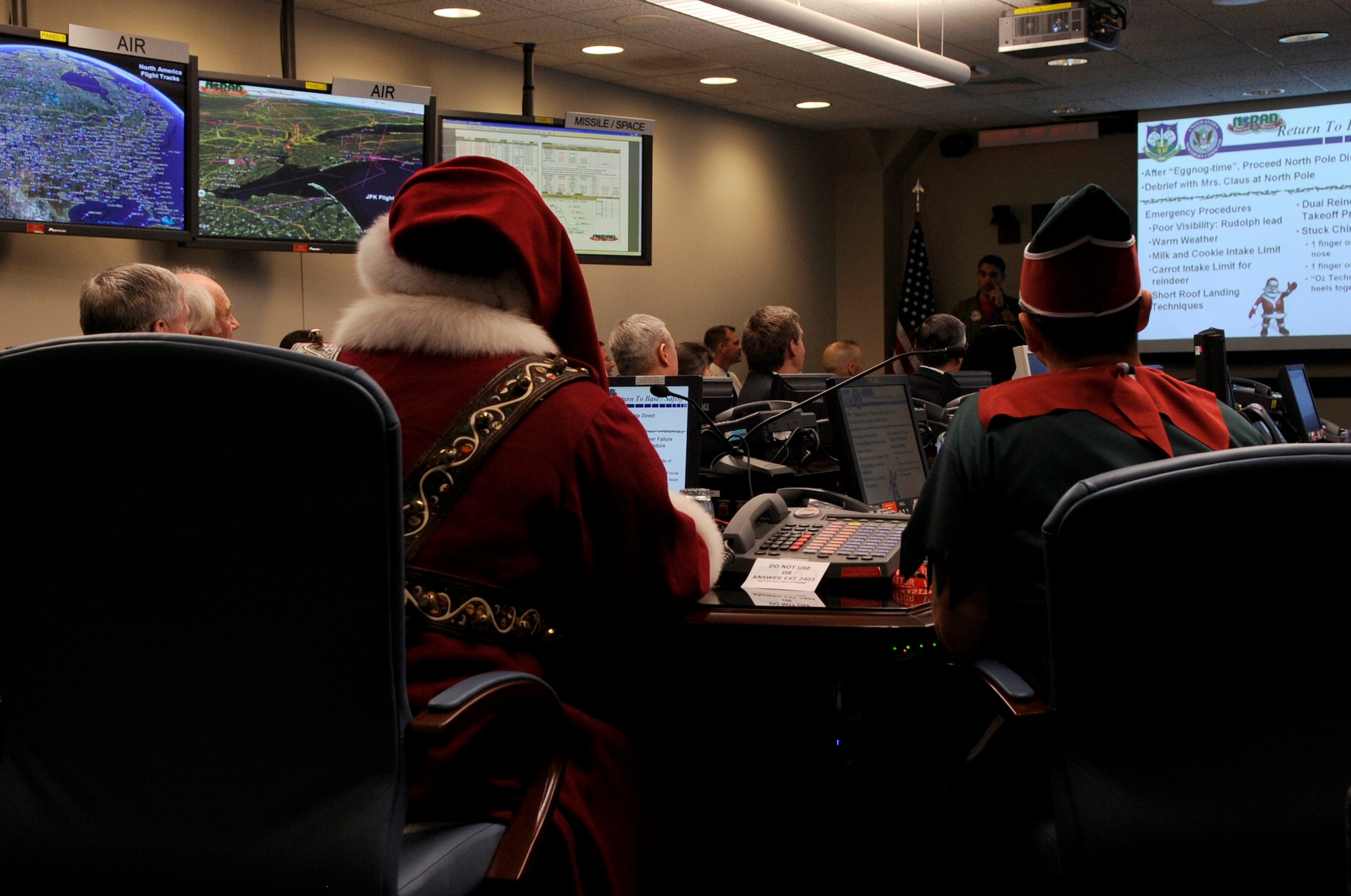 Santa Claus and Elf Dee make a surprise visit to the North American Aerospace Defense Command Tracks Santa Battle Cab Dec. 23 at Peterson Air Force Base, Colo. Santa received Federal Aviation Administration, weather and air mission briefs. (U.S. Air Force photo/Staff Sgt. Desiree N. Palacios) 