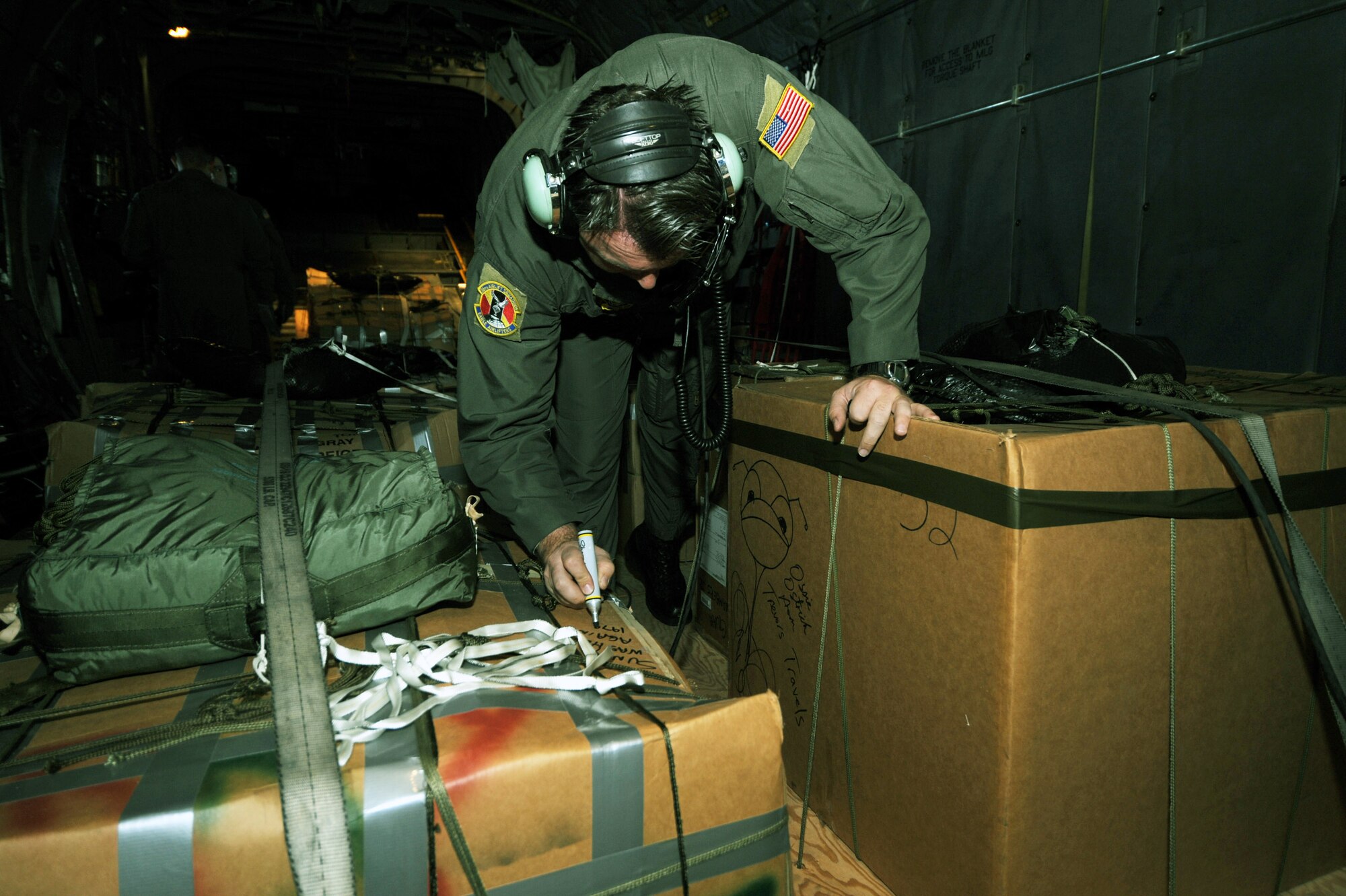 Chief Master Sgt. Michael Sundberg writes a holiday greeting on a pallet of goods to be dropped from a C-130 Hercules during Operation Christmas Drop Dec.19 over the Pacific Ocean. Airmen today continue the tradition, delivering supplies to remote islands of the Commonwealth of the Northern Marianas Islands, Yap, Palau, Chuuk and Pohnpei. More than 600 pounds of donated goods was dropped over the remote islands during the operation. Chief Sundberg is a loadmaster from the 36th Airlift Squadron from Yokota Air Base, Japan.  (U.S. Air Force photo/Master Sgt. Kevin J. Gruenwald)