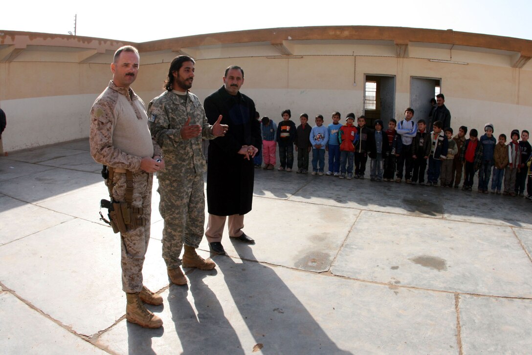 With the assistance of "Rock" (center), a Jordanian interpreter, 1st Sgt. Clark Rhiel (left), the first sergeant for Headquarters and Service Company, 2nd Battalion, 25th Marine Regiment, Regimental Combat Team 5, speaks to second grade students at Mekasid Primary School in Rutbah, Iraq, Dec. 23. The Marines and sailors of 2nd Bn, 25th Marines visited the school to distribute toys and snacks sent by patriotic Americans.::r::::n::